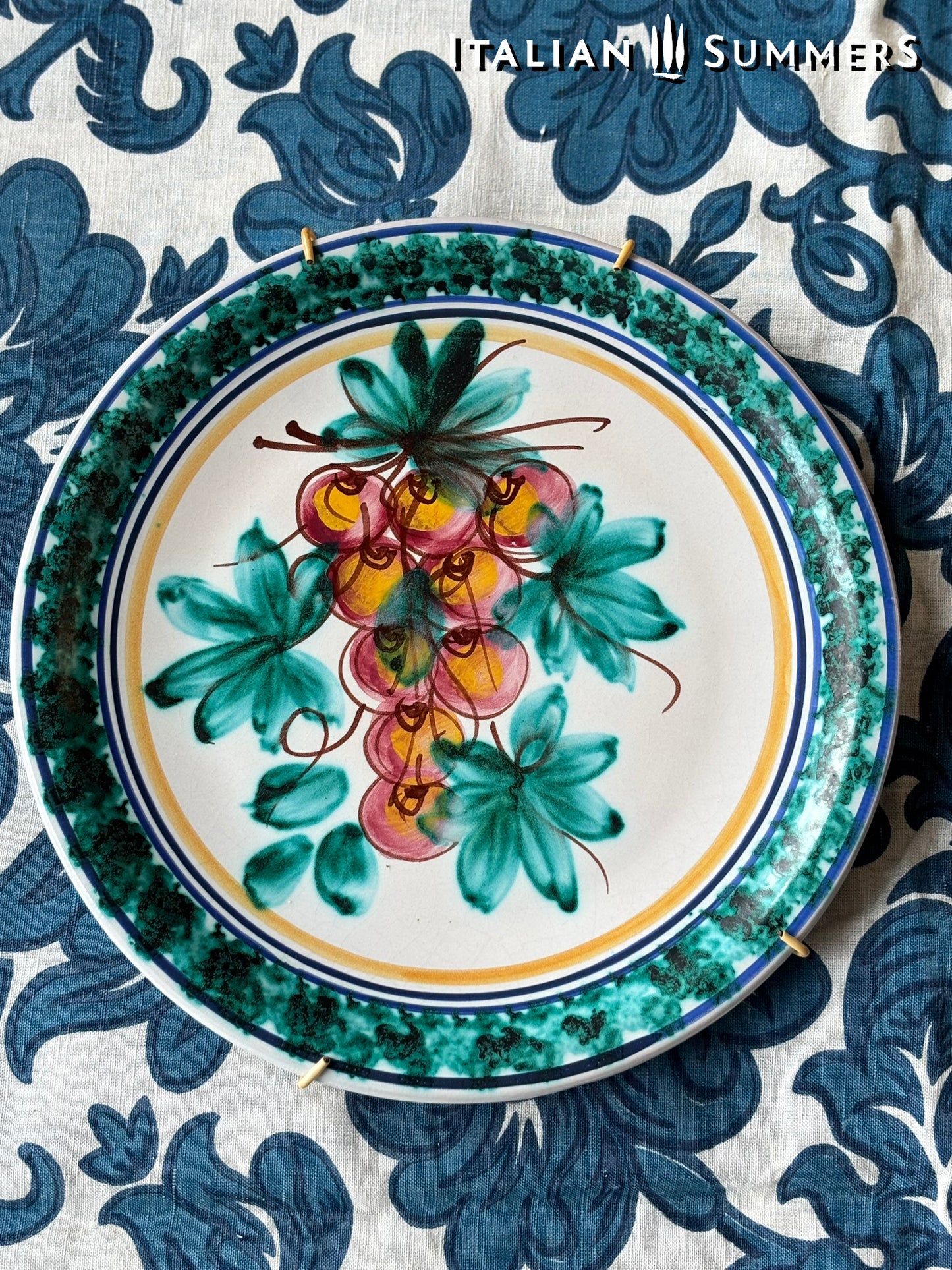Decorative Sicilian Caltagirone  plate with leaf and fruit design on a blue and white patterned fabric background.