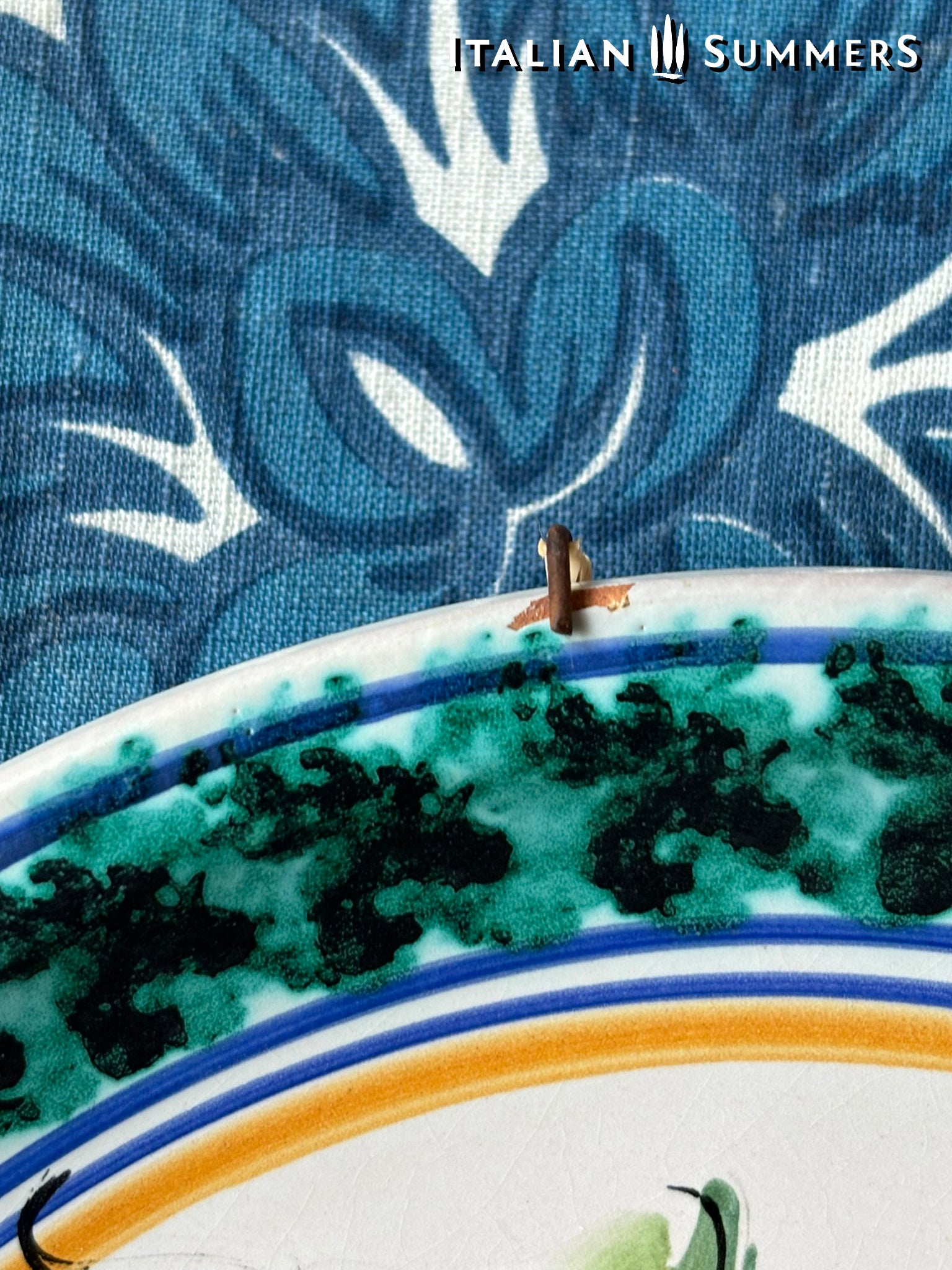 detail of rim of a Sicilian Decorative plate with blue and green patterns on a textured fabric background