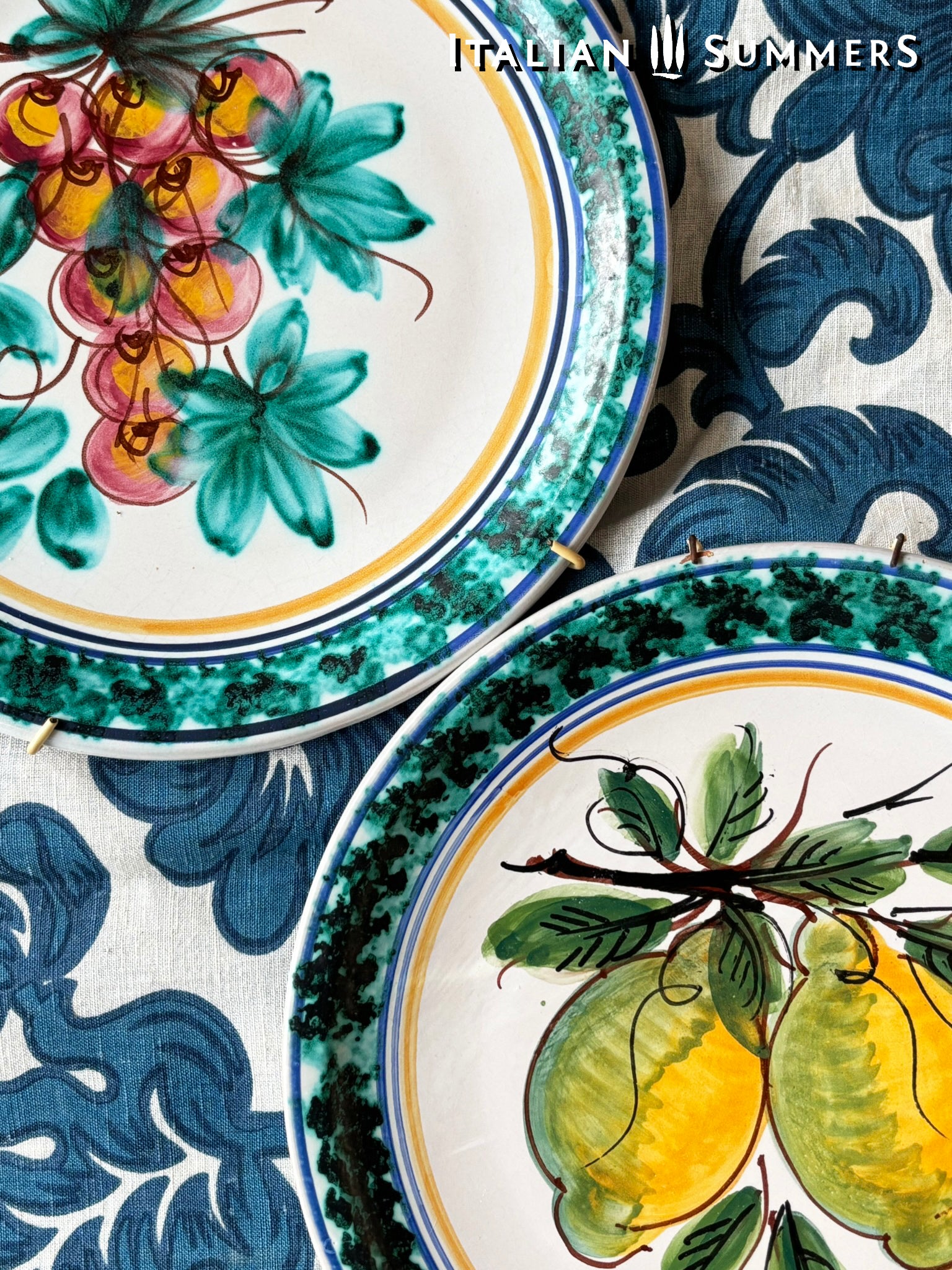 Decorative Sicilian Caltagirone maiolica ceramic plates with floral and fruit designs on a patterned background, featuring the brand 'Italian Summers'.