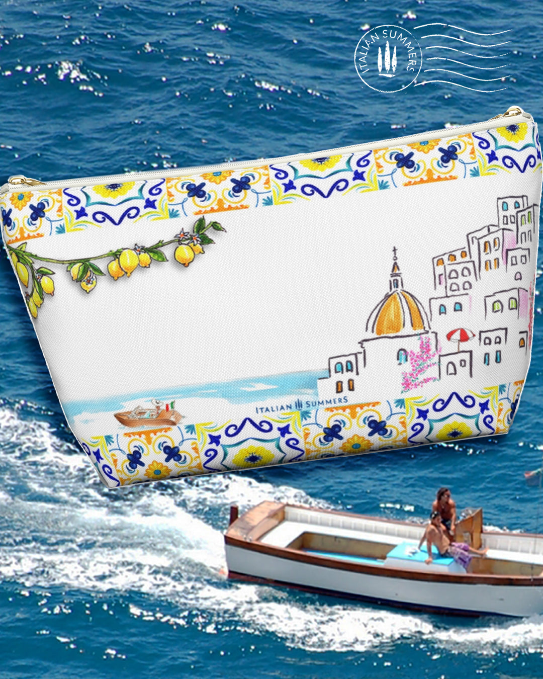 An Italy inspired white canvas clutch with the text Find me in Italy. On the front ther is a sketch of a lady on a striped beach towel under a blue and white beach umbrella seen from above. On the top and bottom there is a rim with blue and yello Italian tiles. In the back there is a sketch of Positano and a Riva boat in the sea. Front and back have also some lemon branches. Designed by Italian Summers