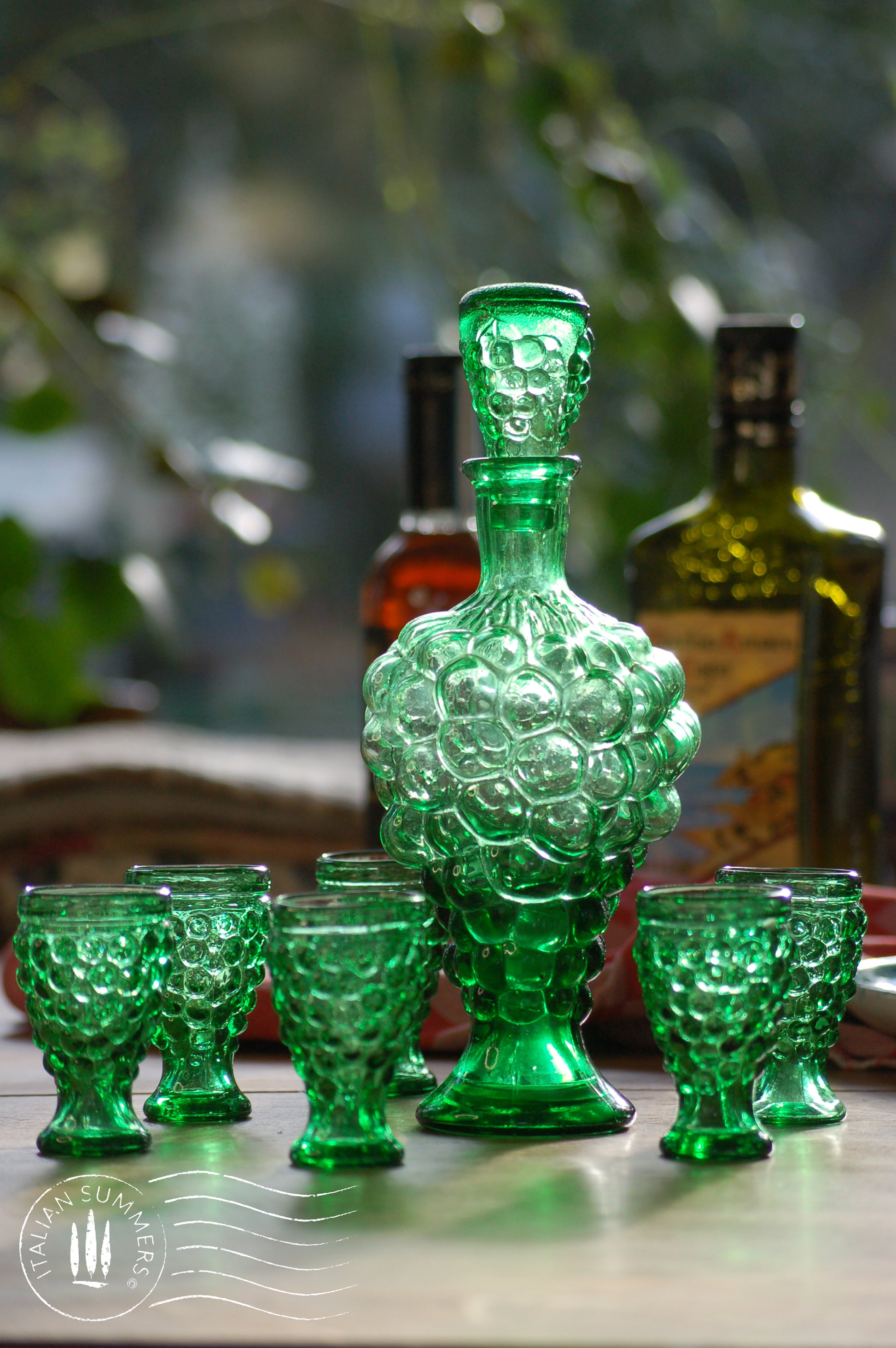 Green empoli emerald green glass decanter and tumblers with bottles in the background
