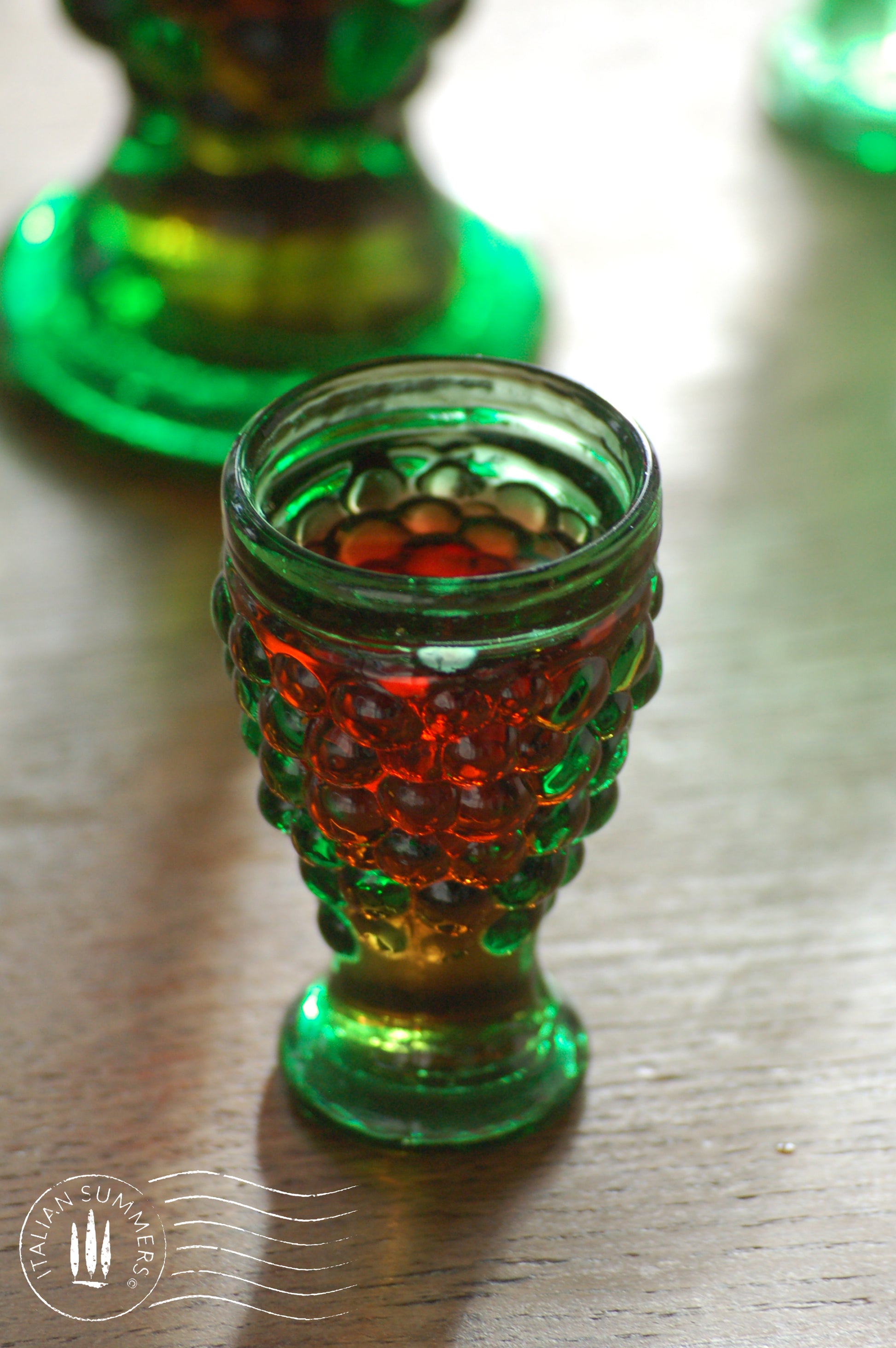 emerald Green glass goblet with red liquid on a wooden surface