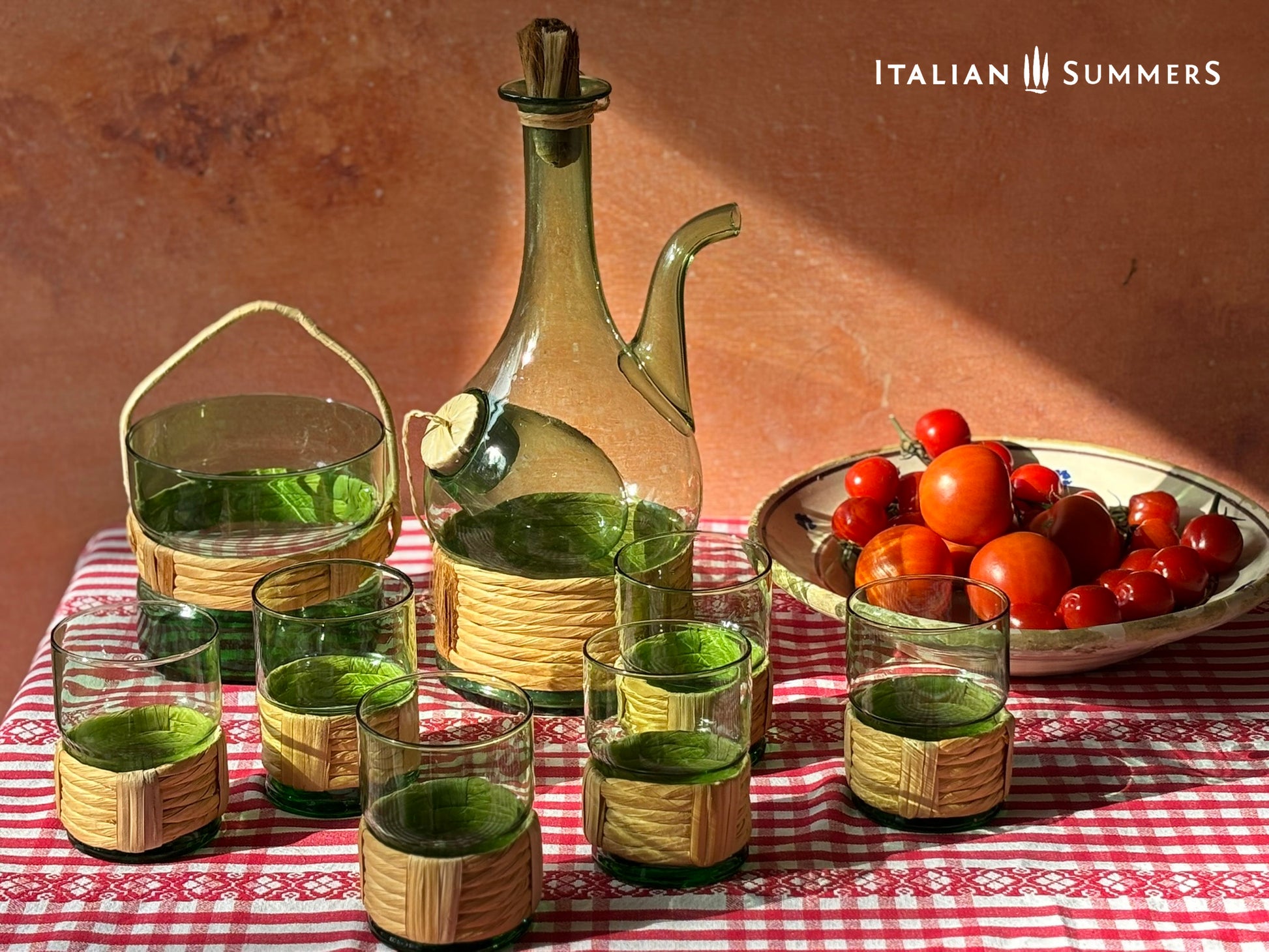 Green Empoli vintage glassware and decanter on a table with a checkered tablecloth, tomatoes, and 'Italian Summers' branding.