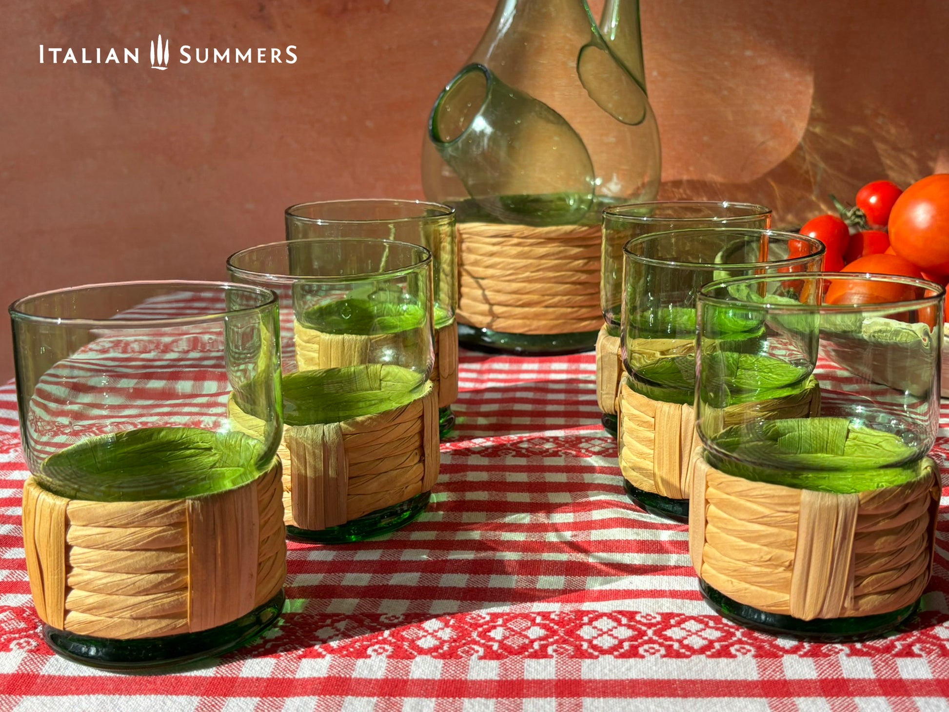 Green Empoli vintage glassware and decanter on a table with a checkered tablecloth, tomatoes, and 'Italian Summers' branding.
