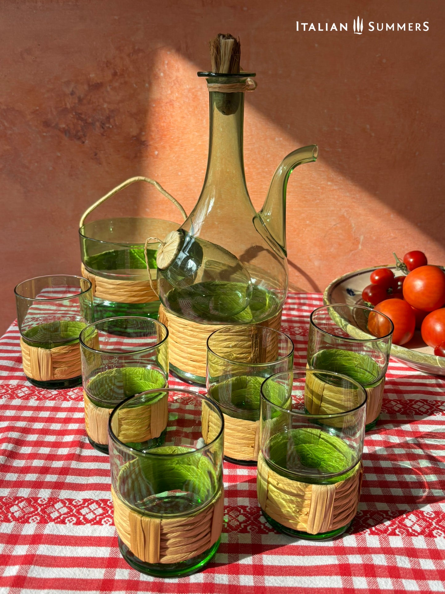 Green Empoli vintage glassware and decanter on a table with a checkered tablecloth, tomatoes, and 'Italian Summers' branding.