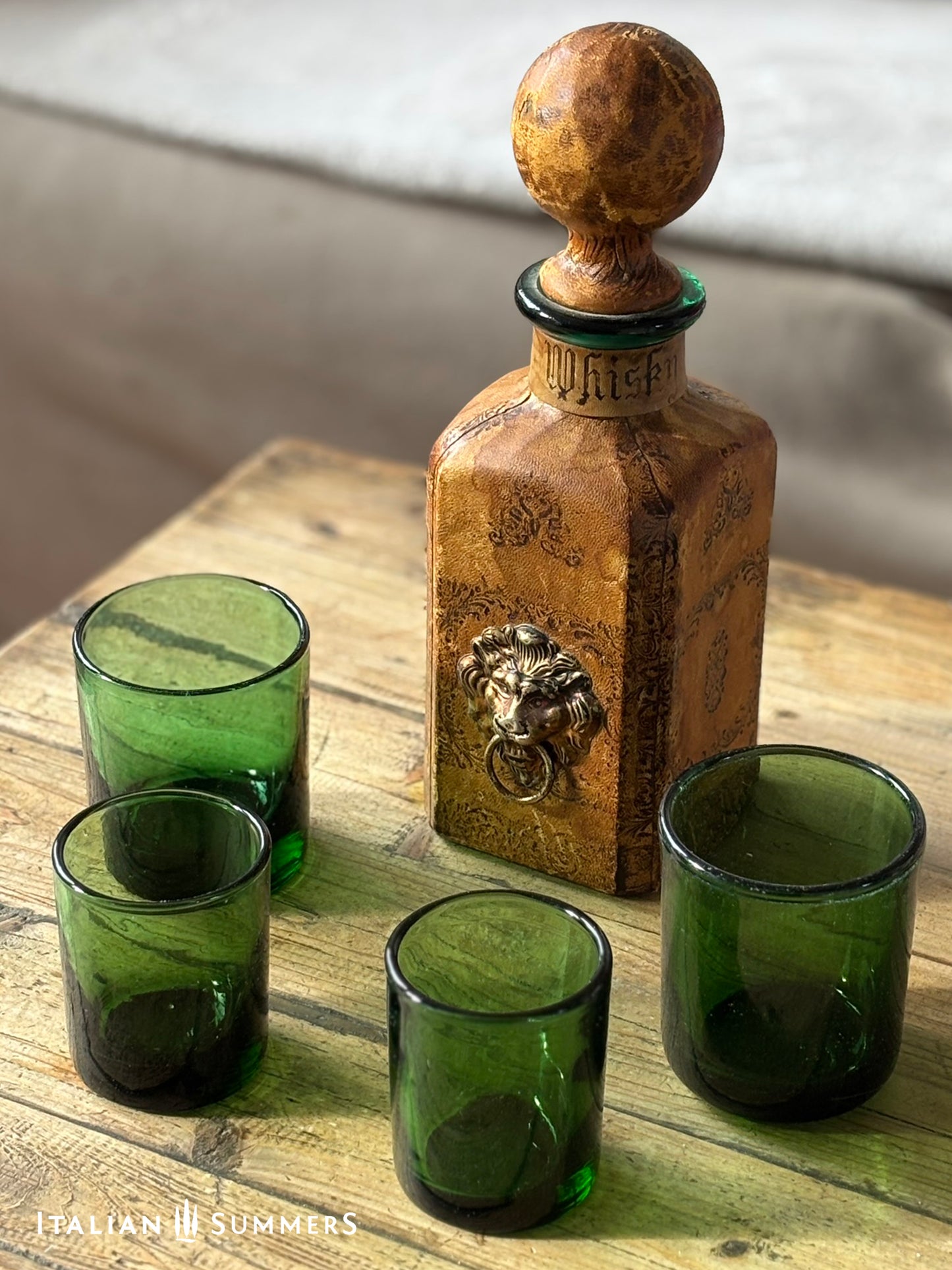 vintage leather-covered decanter with a lion emblem and green glass tumblers on a wooden surface.