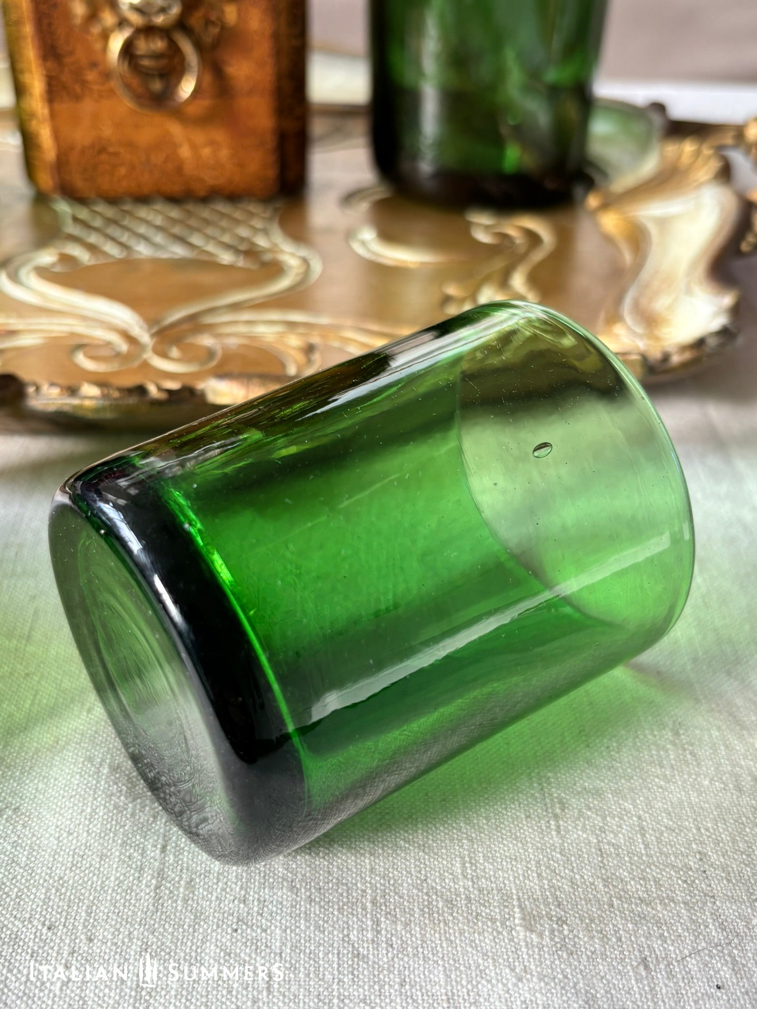 Vintage Emerald-Green glass tumbler on a textured surface with decorative items in the background