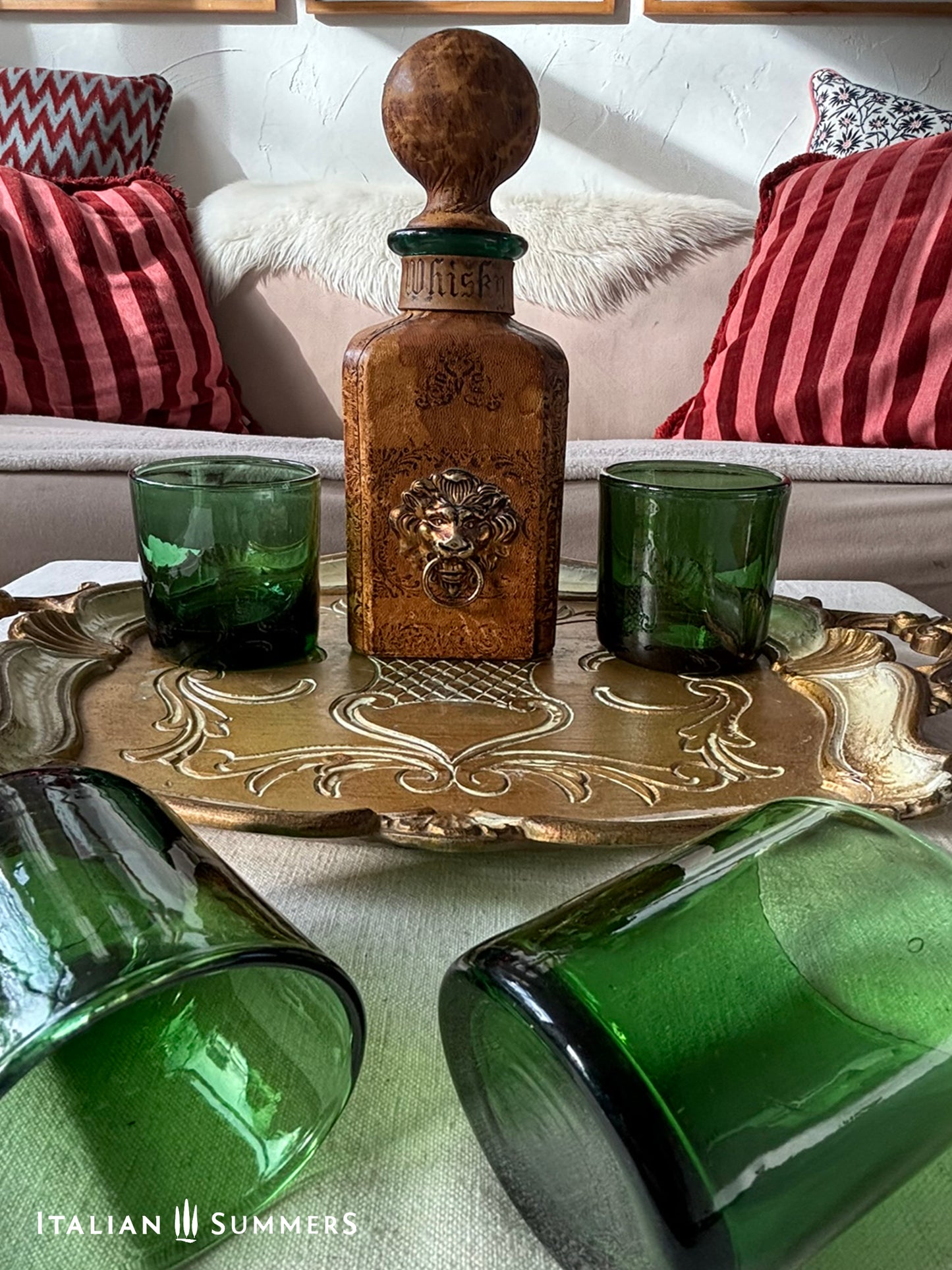 Decorative leather-covered Florentine whiskey decanter with green glass cups on a gold tray in a living room setting.
