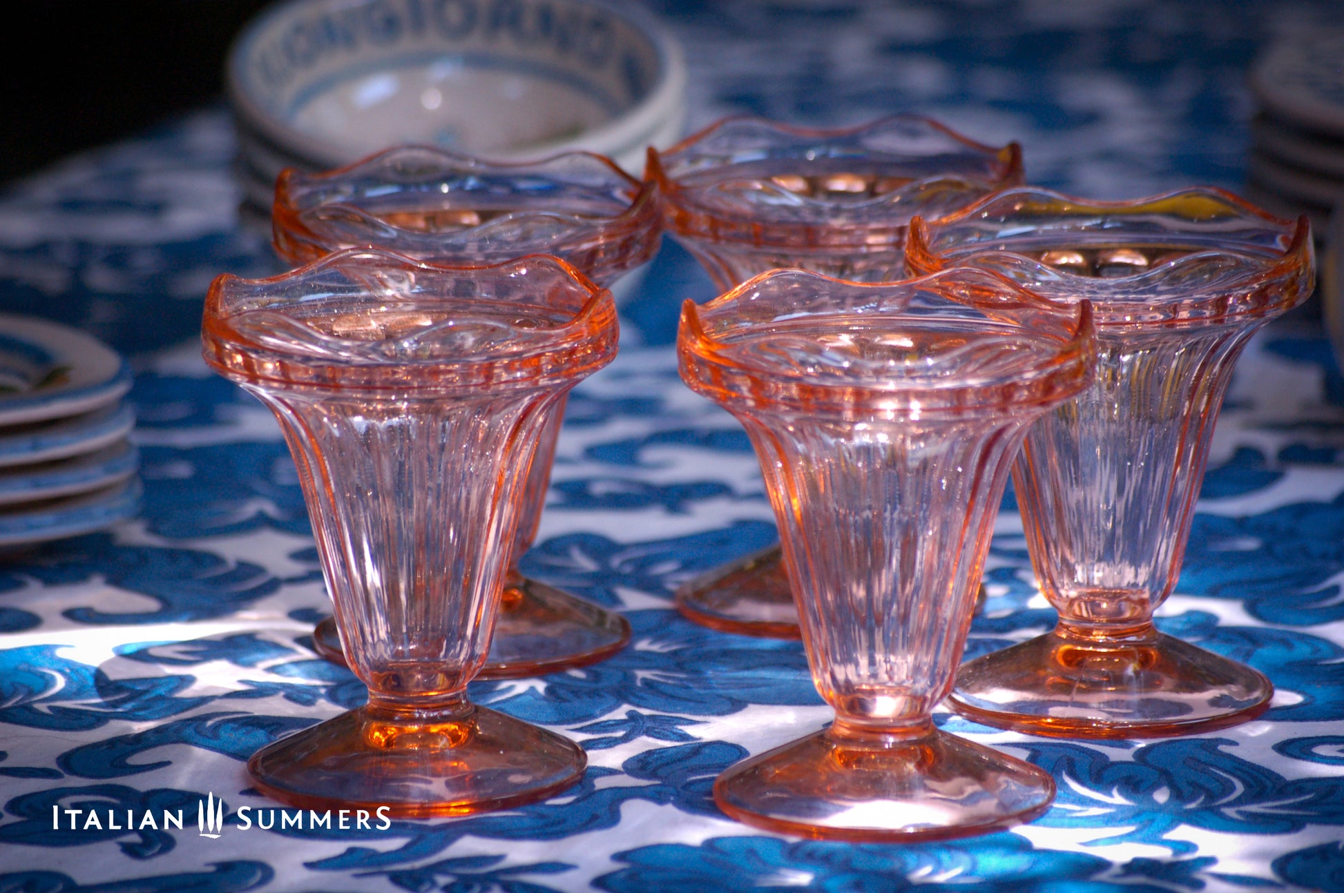 Set of pink glass dessert dishes on a blue patterned tablecloth with 'Italian Summers' branding.