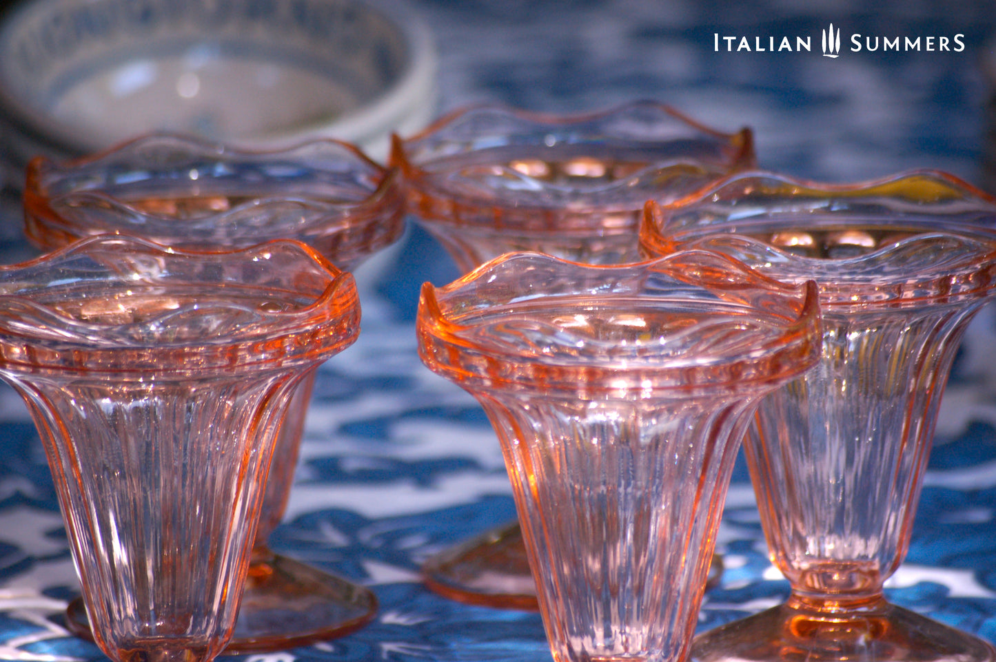 Set of rose glass dessert coupes on a blue patterned surface with 'Italian Summers' branding.