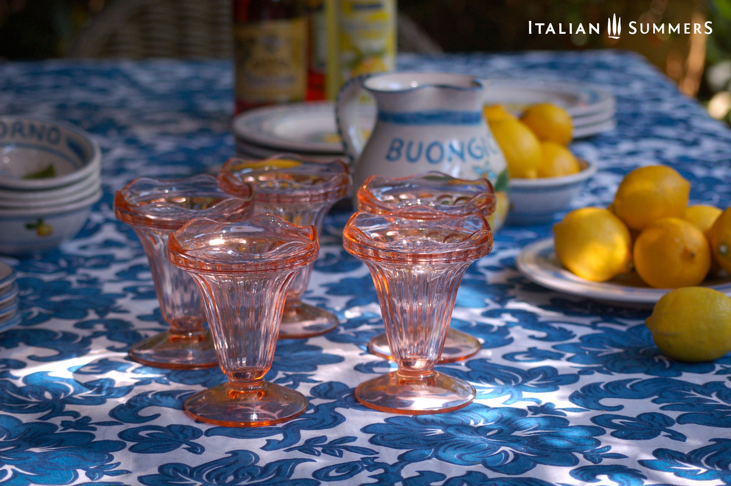 Pink glassware on a table with lemons and 'Buongiorno' cups, set against an Italian Summers backdrop.