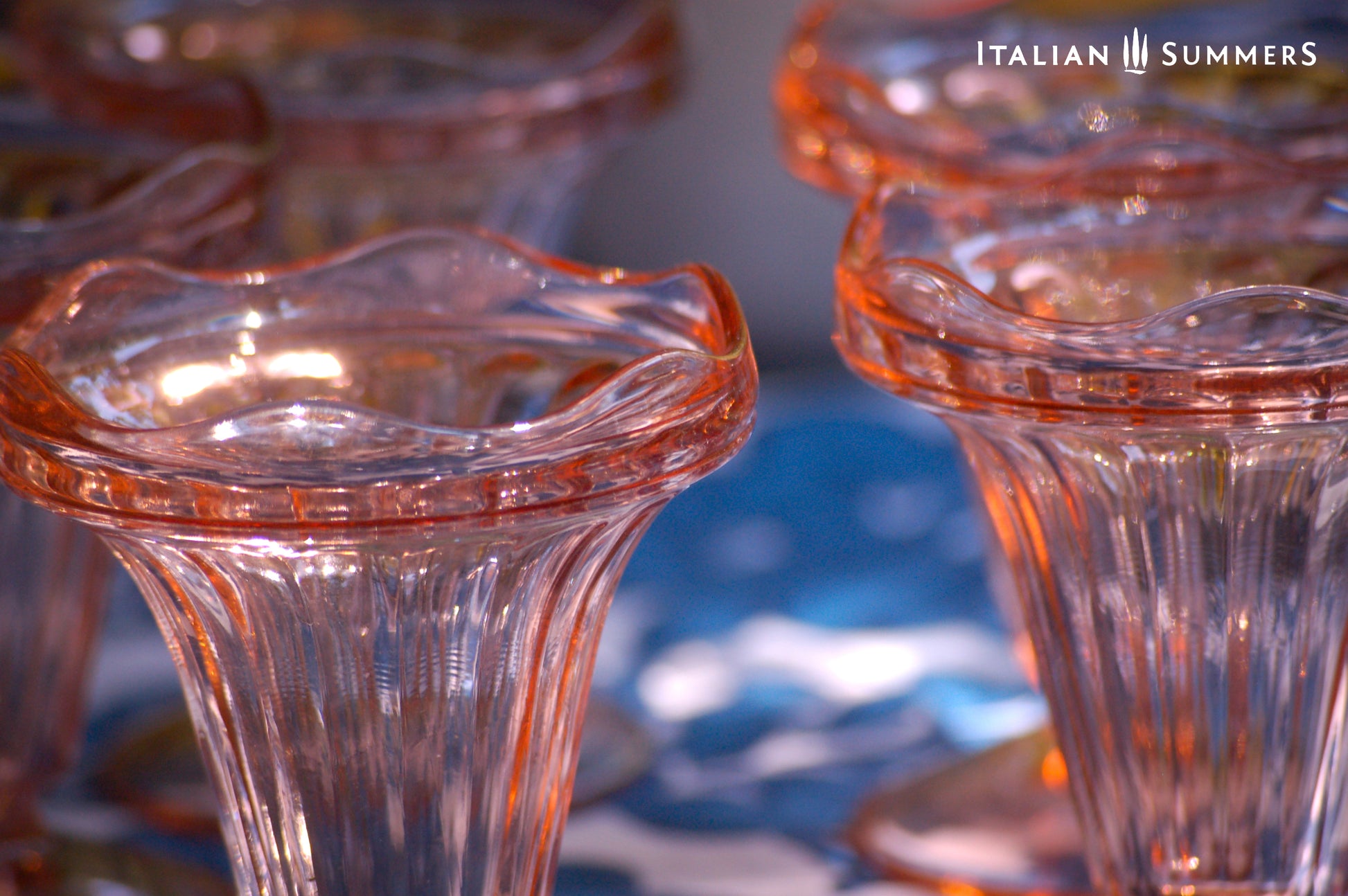 Close-up of Set of vintage French pink glass dessert coupes  on a blue and white floral patterned tablecloth
