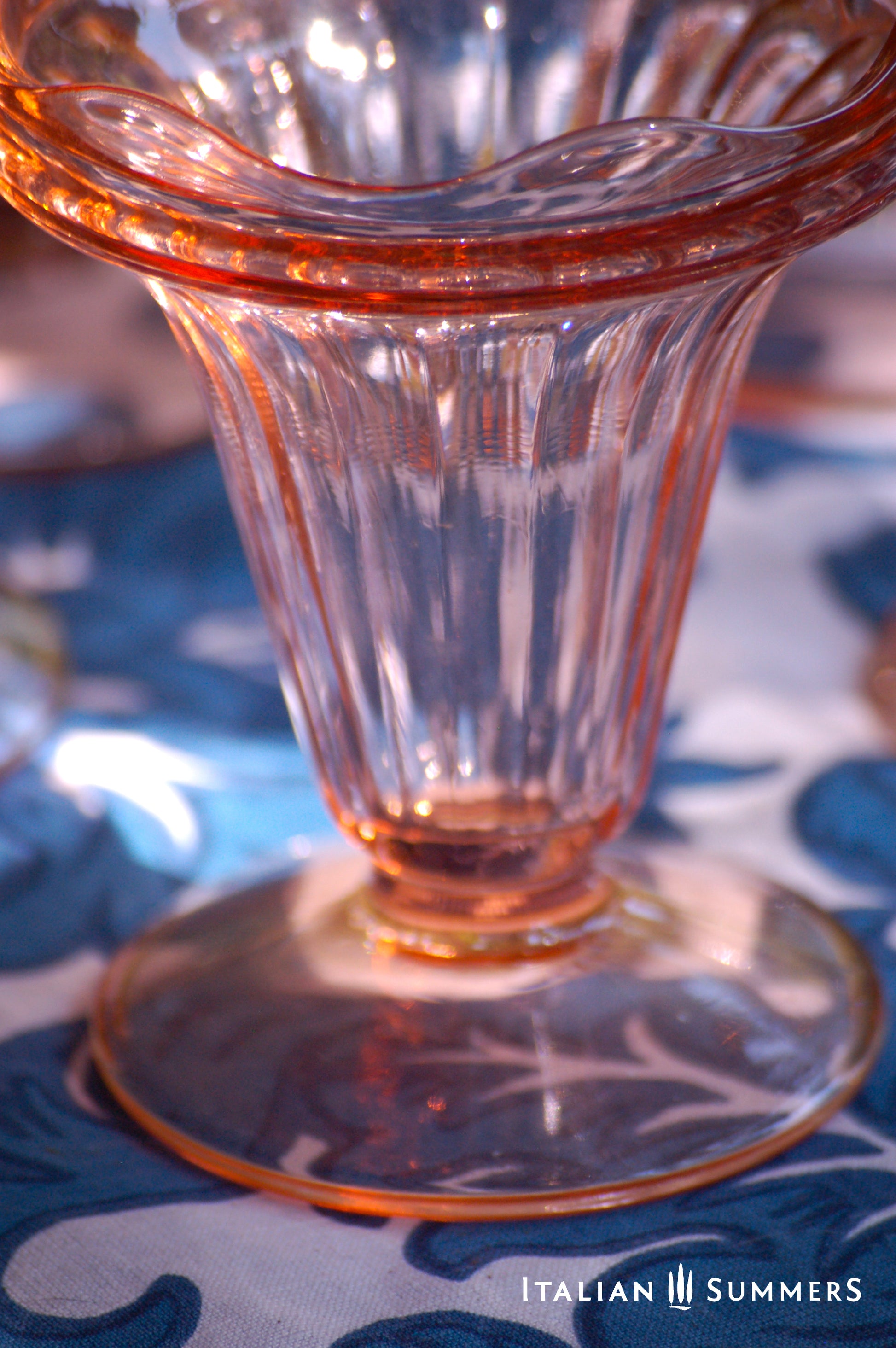 Close up of a vintage French pink glass dessert coupe  on a blue and white floral patterned tablecloth
