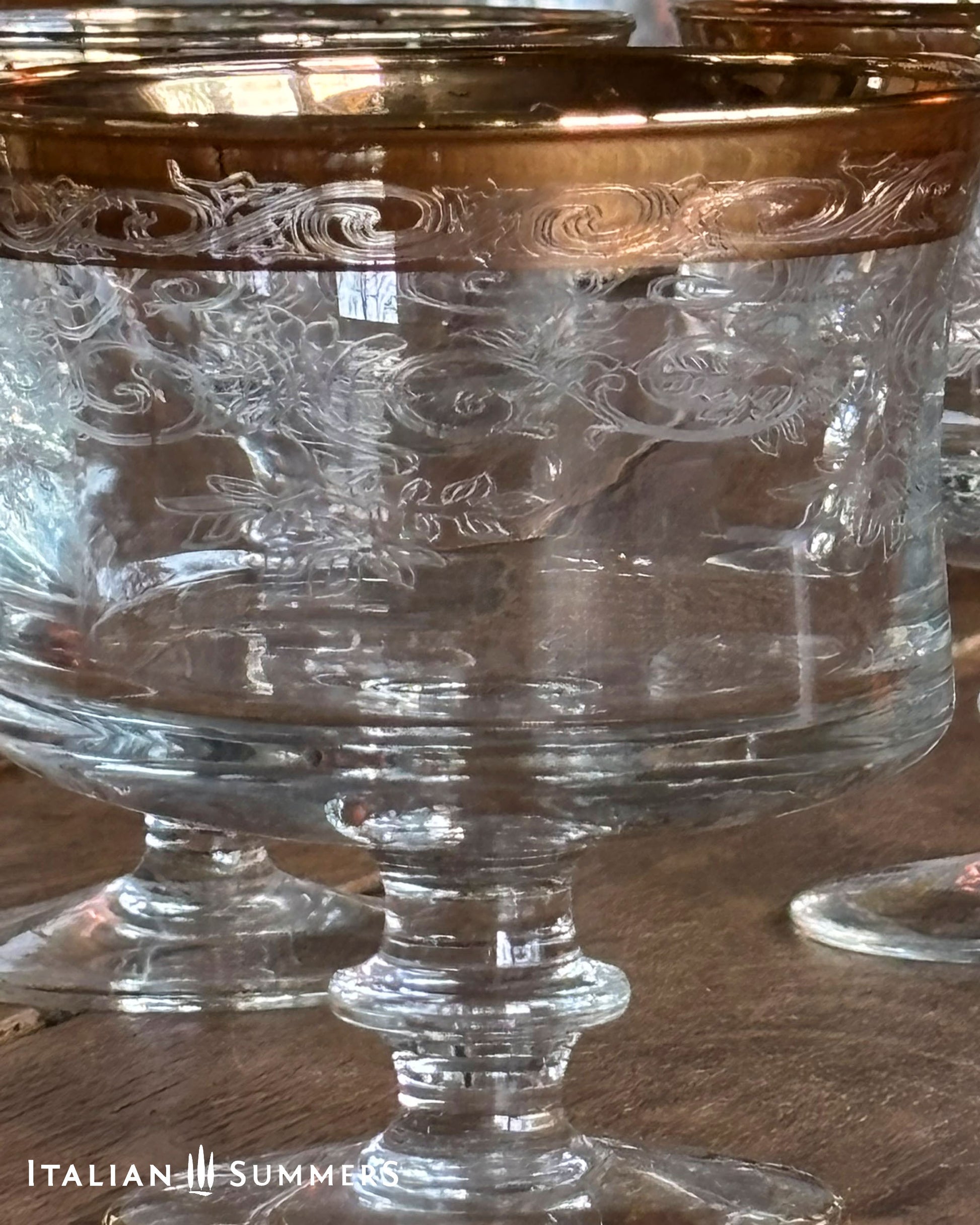 Clear glass goblets with gold rims on a wooden surface, branded 'Italian Summers'.