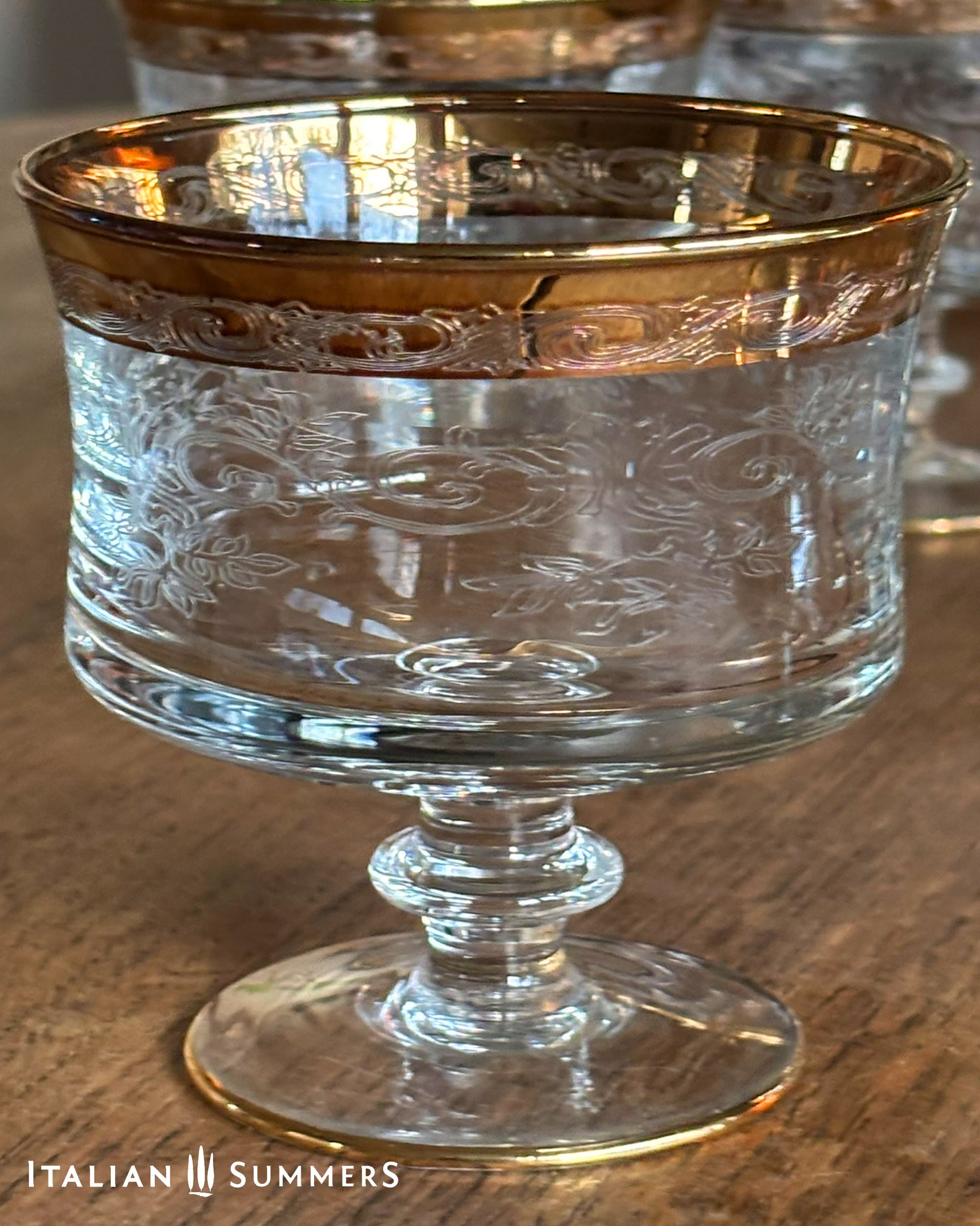 Clear glass with gold rim on a wooden surface, branded 'Italian Summers'.