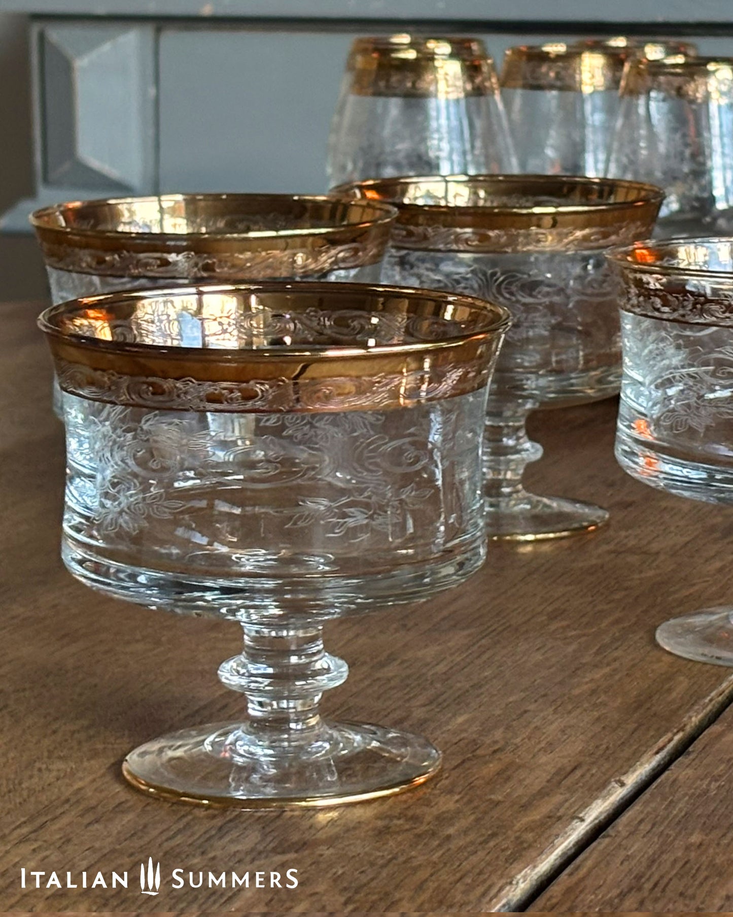 Clear glass goblets with gold rims on a wooden surface, branded 'Italian Summers'.