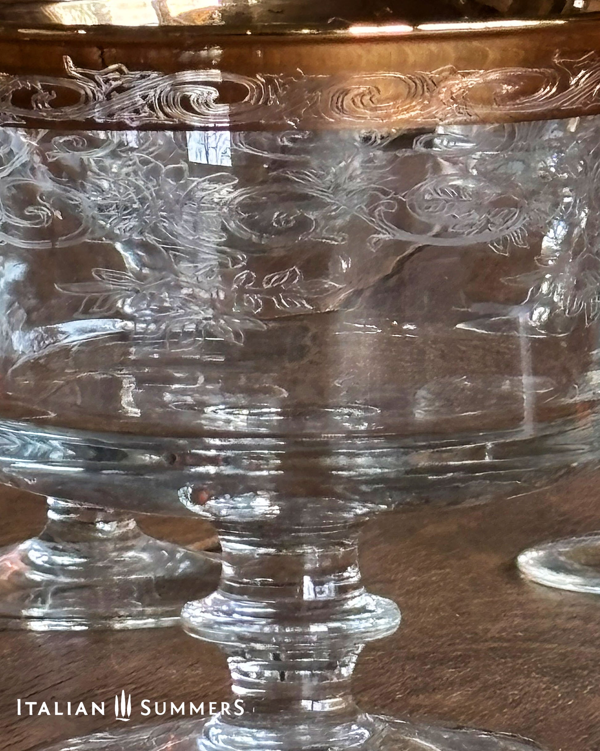 Clear glass coupes with engraved patterns and gold rims on a wooden surface, branded 'Italian Summers'.