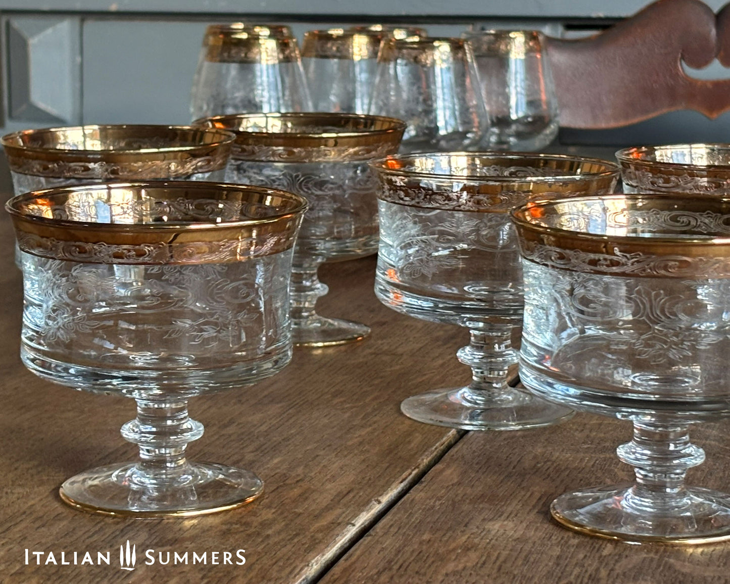 Set of clear glass goblets with gold rims on a wooden surface, brand 'Italian Summers' visible.
