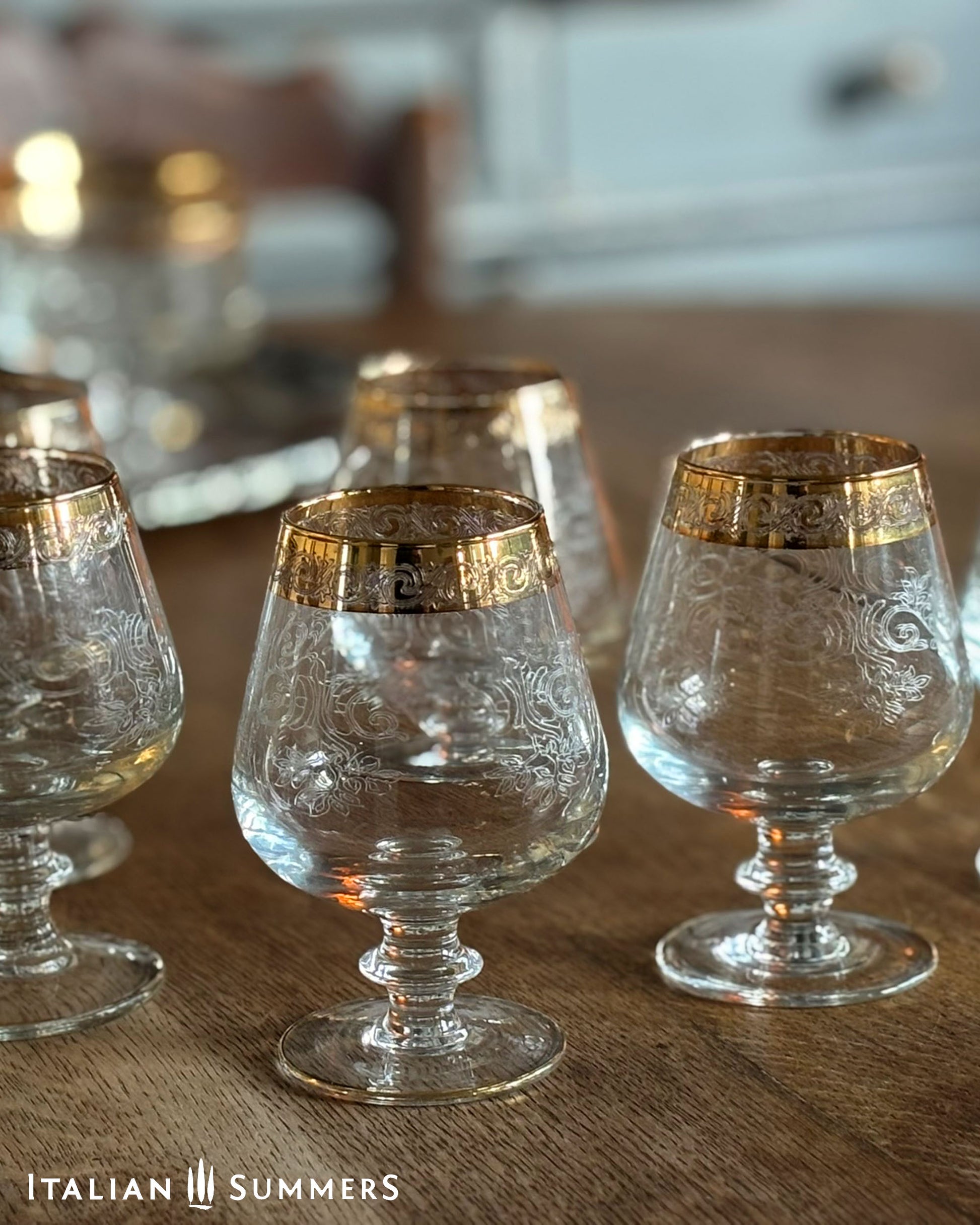 Set of ornate glass tumblers with gold rims on a wooden surface, branded 'Italian Summers'.