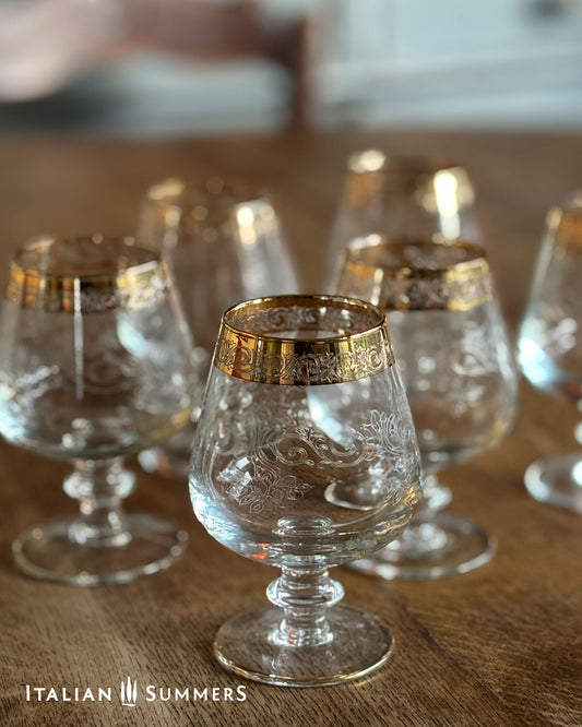 Set of clear glass goblets with gold rims on a wooden surface, branded 'Italian Summers'.
