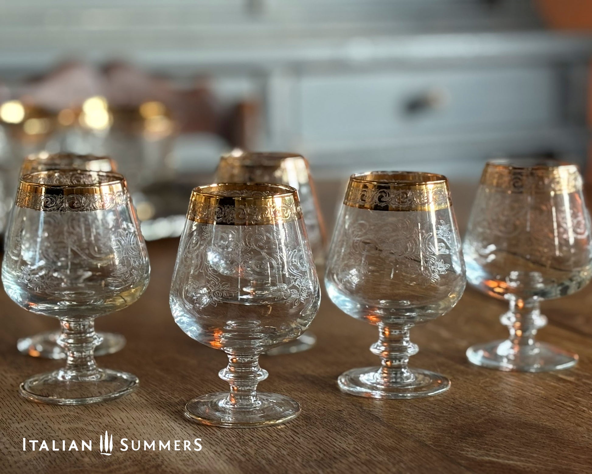 Set of clear glass goblets with gold rims on a wooden surface, branded 'Italian Summers'.