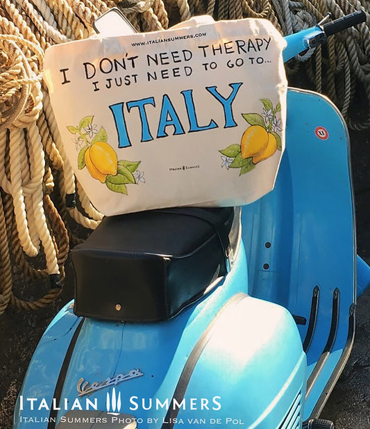 Tote bag with the quote " I don't need therapy, I just need to go to Italy " sitting on a vintage blue Vespa.  The quote is flanked by Amalfi lemons with flowers. Designed and sold by Italian Summers
