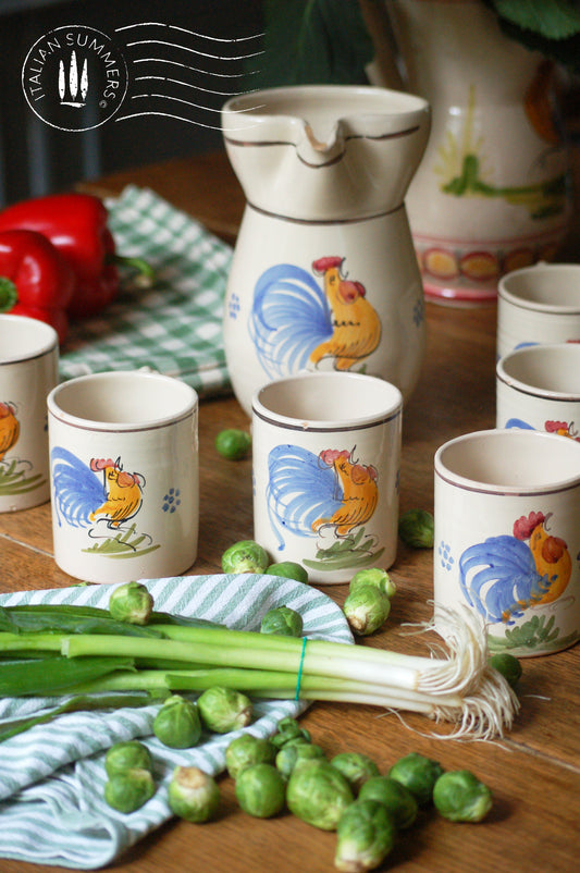 A set of Vintage maiolica ceramic six mugs and a carafe from Puglia, Italy. Each mug as well as the carafe are glazed with the traditional creamy white Grottaglie glaze, decorated with a hand-painted colorful rooster, symbol of good luck and prosperity. 