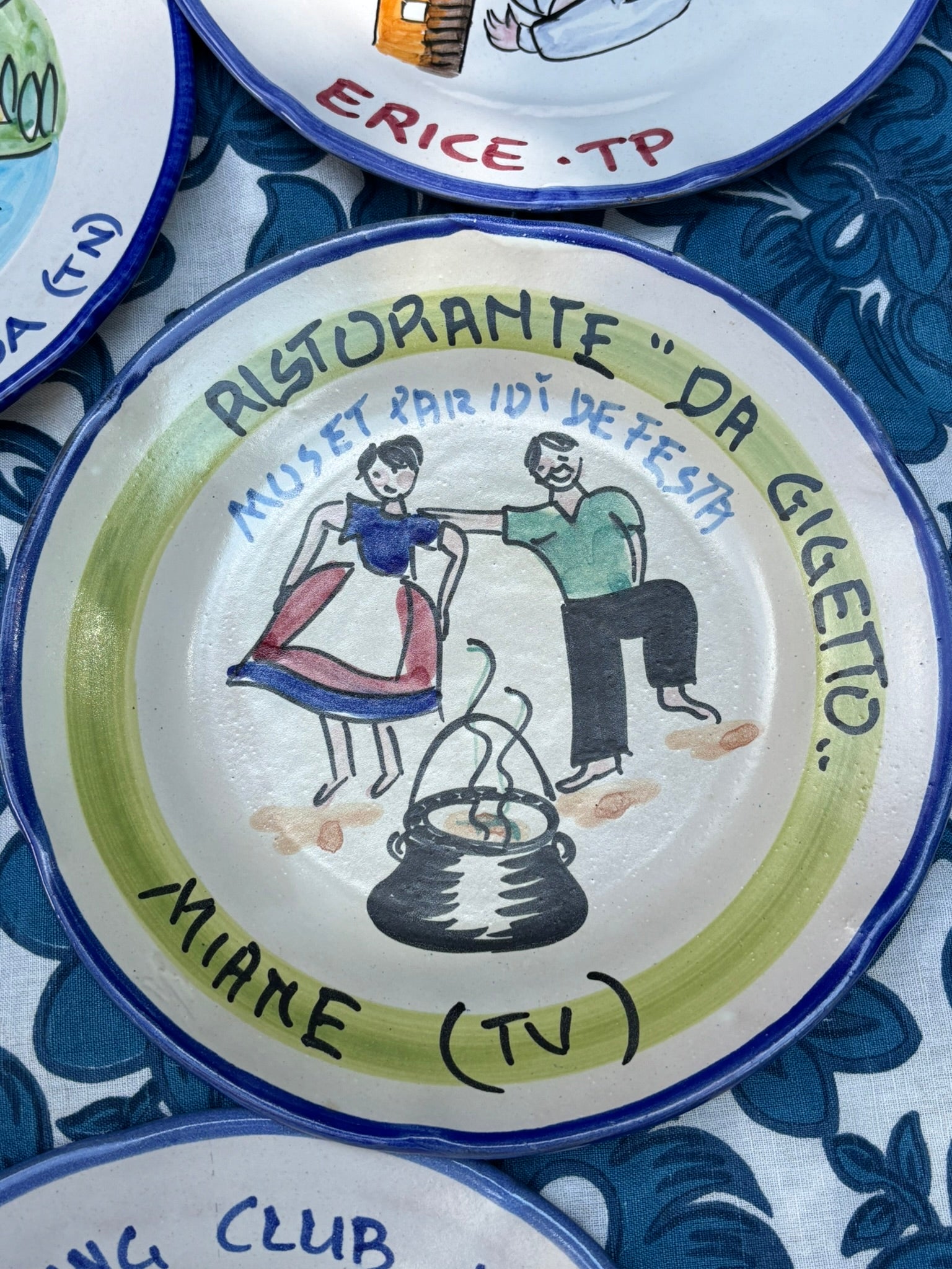 Italian ceramic plate with artistic depiction of a couple and Italian text Ristorante Da Gigetto, placed on a patterned tablecloth