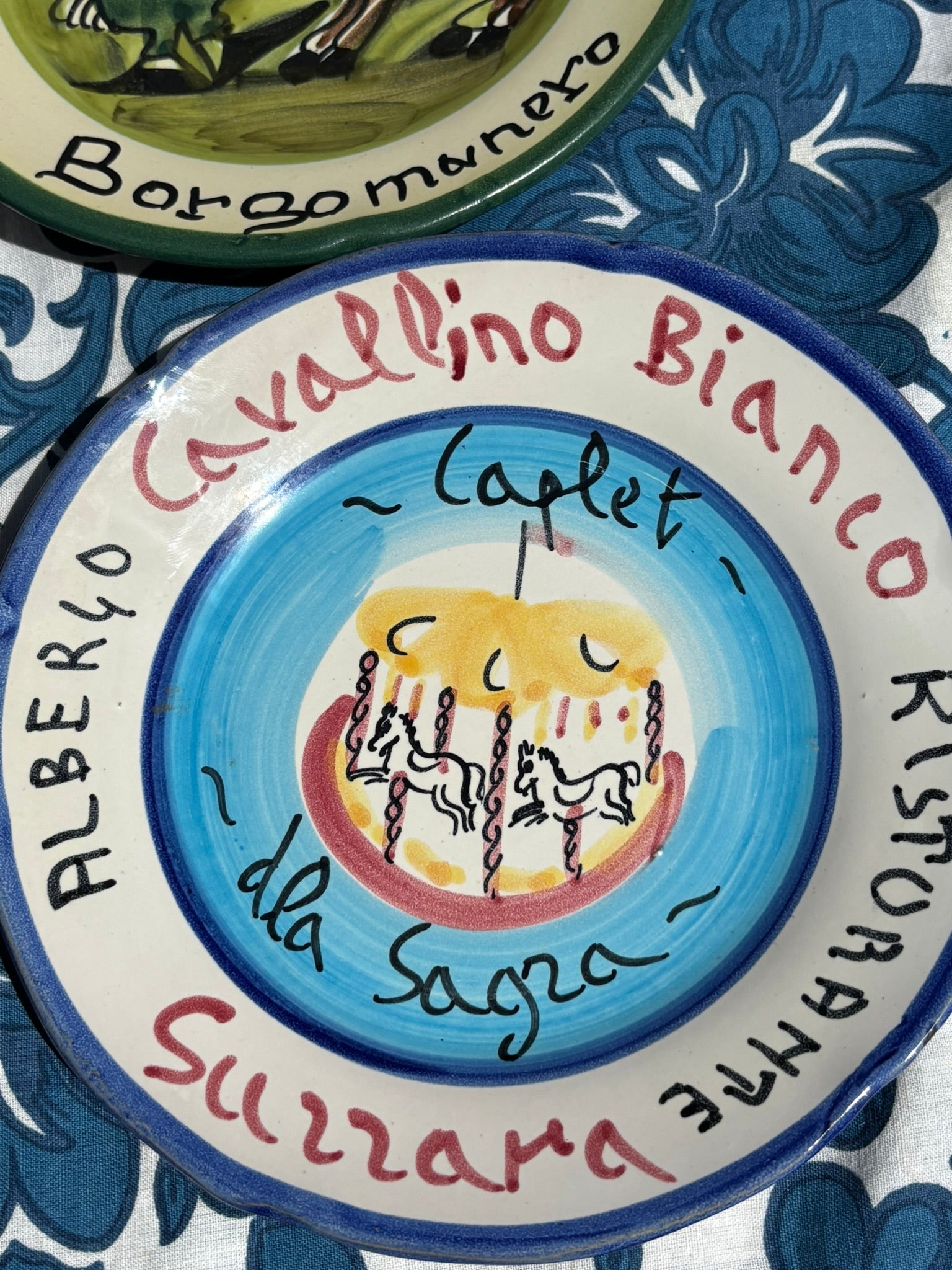 Decorative  Italian ceramic vintage plate with Italian text and a graphic design on a blue and white patterned tablecloth