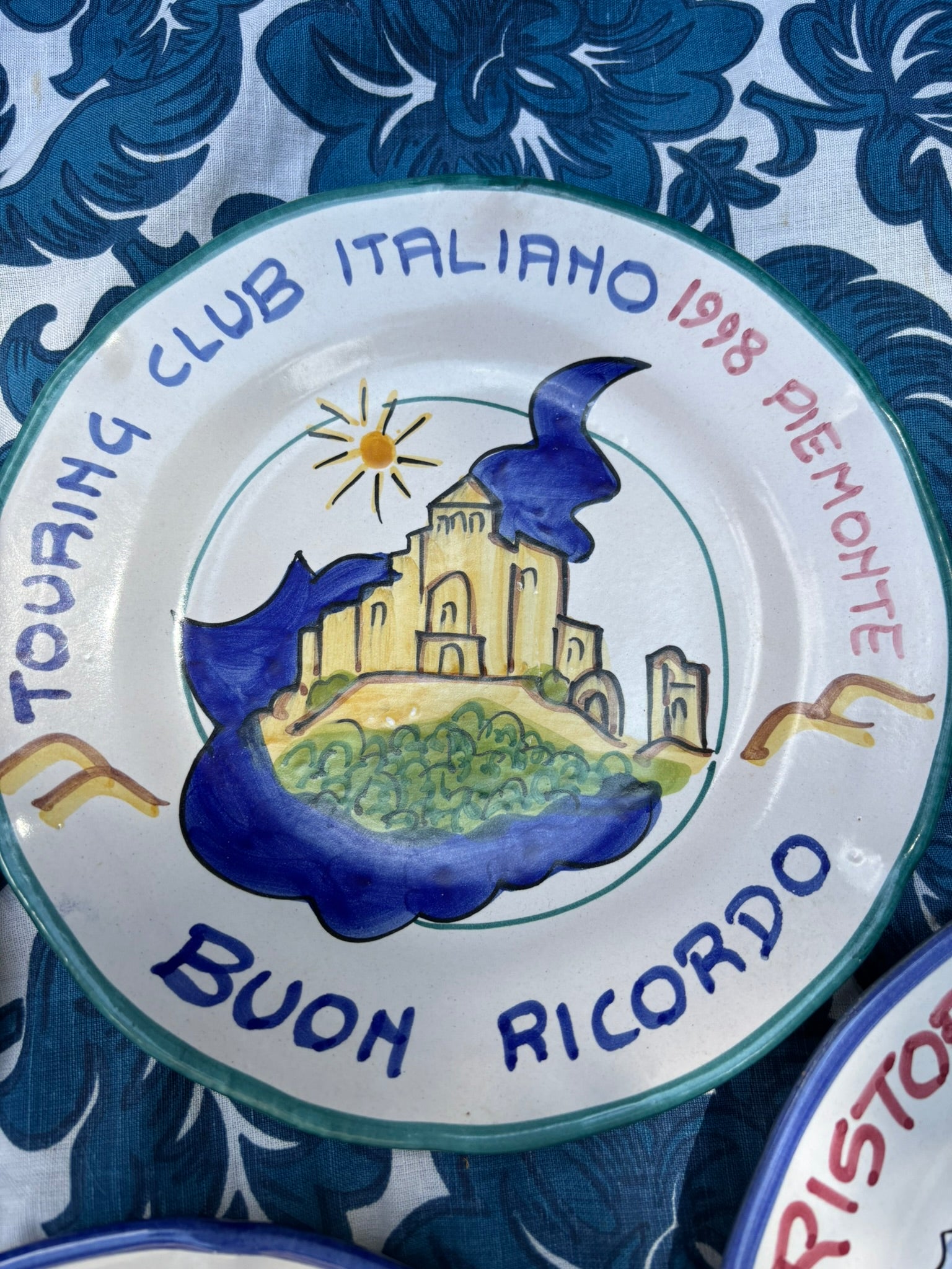Italian ceramic plate with Italian text  Touring club Italiano and handpainted  castle illustration on a blue floral table cloth