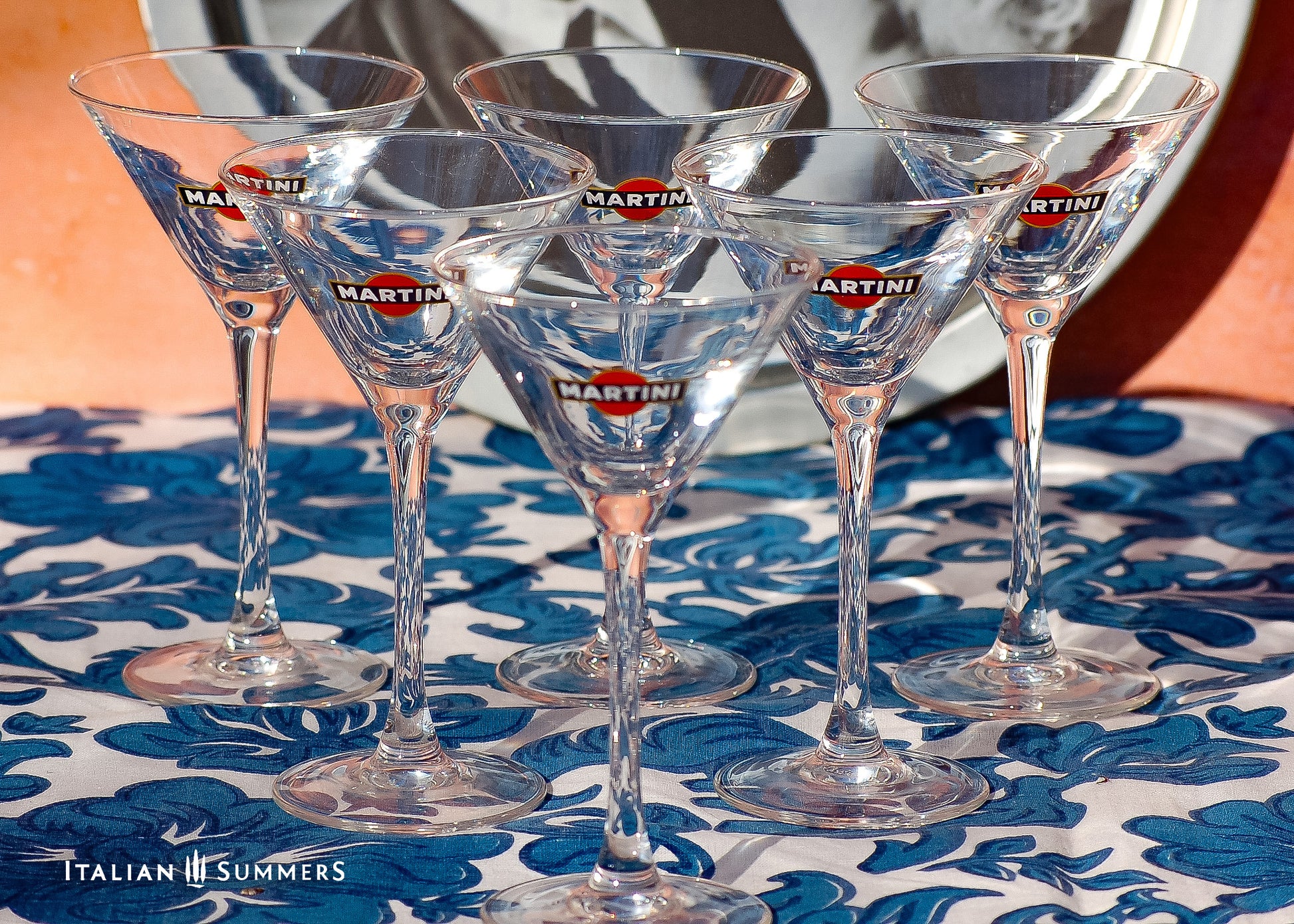 Set of Martini glasses on a floral tablecloth with 'Italian Summers' branding.