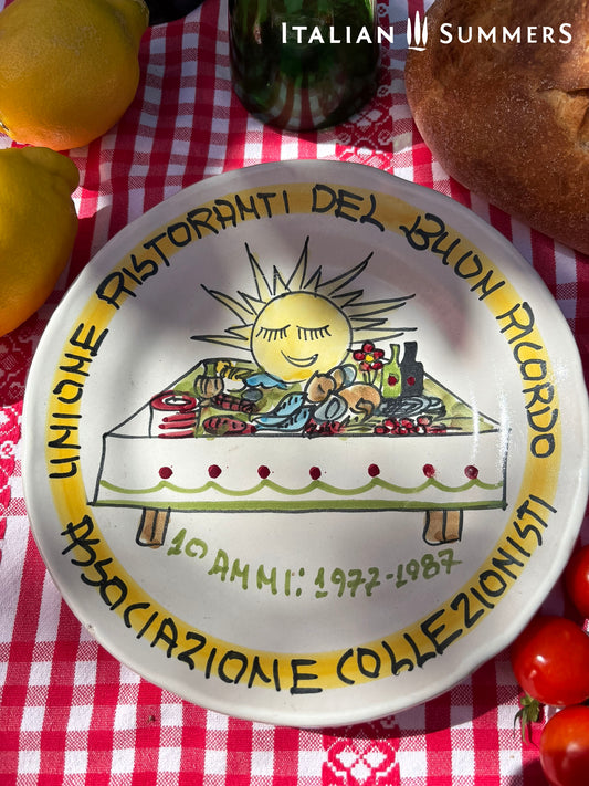Italian Decorative plate with Italian food design on a red and white checkered tablecloth with fruits and bread.