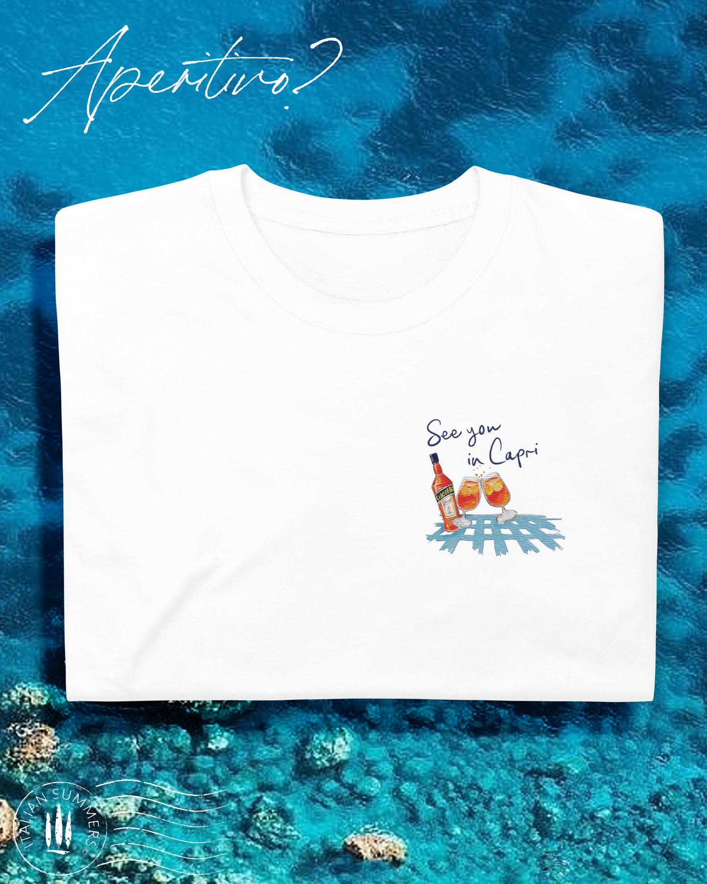 White cotton T shirt with an embroidered illustration on the left chest of two Aperol Spritz glasses in red-orange colors and a Aperol bottle on a blue checkered tablecloth. Above, a Navy blue embroidered quote: See you in CAPRI