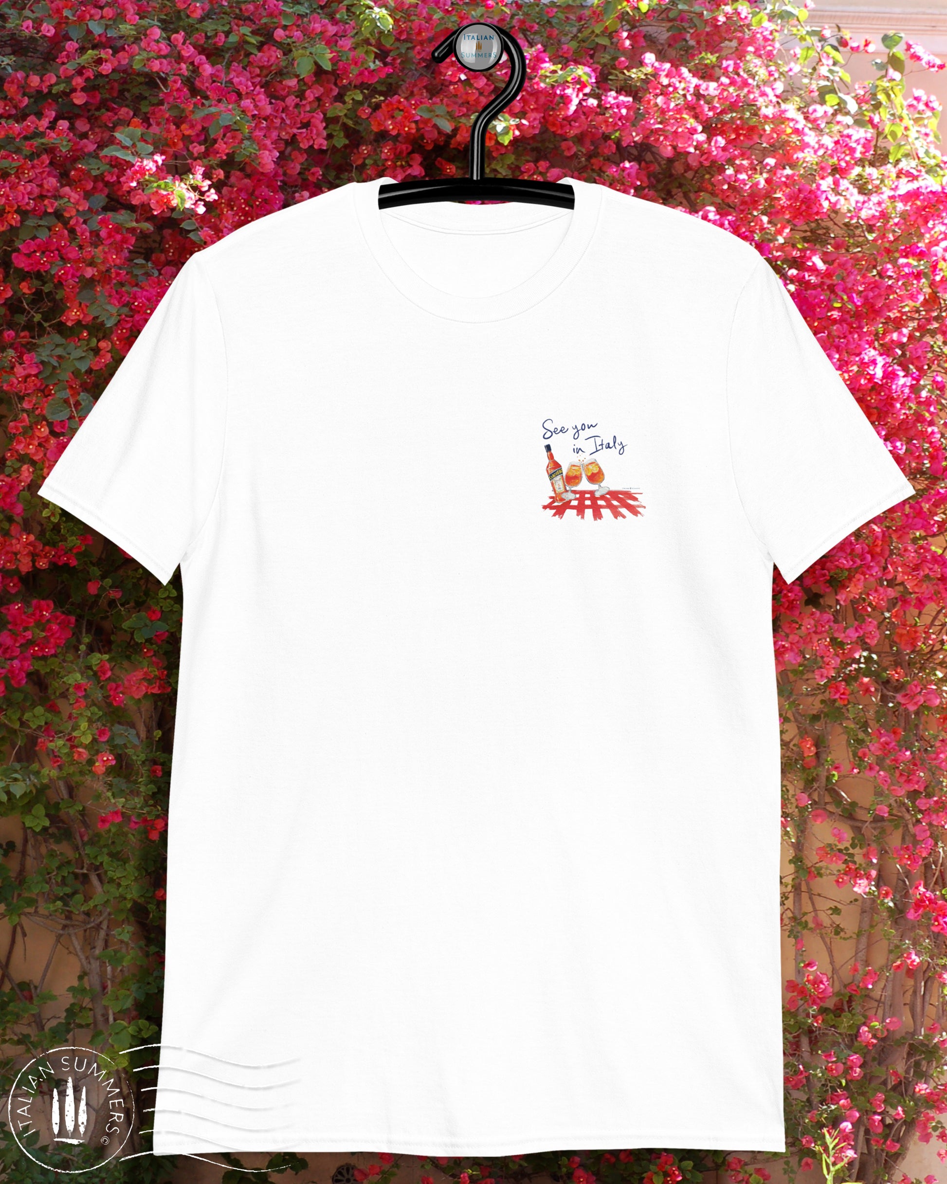 White cotton T shirt with an embroidered illustration on the left chest of two Aperol Spritz glasses in red-orange colors and a Aperol bottle on a red checkered tablecloth. Above, a Navy blue embroidered quote: See you in Italy Desgned and sold by Italian Summers