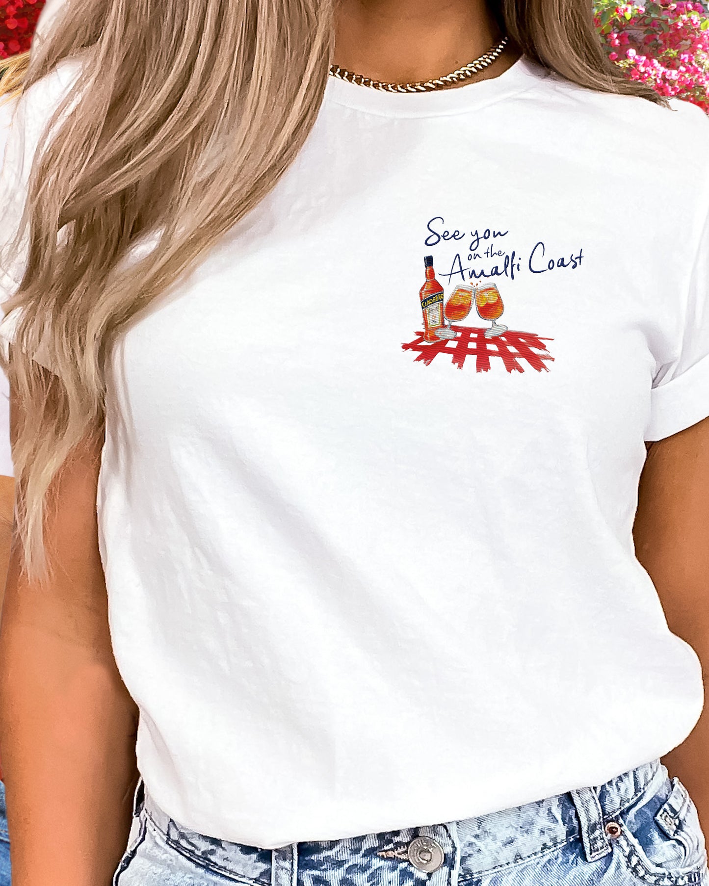 See you on thr Amalfi CoastWhite cotton T shirt with an embroidered illustration on the left chest of two Aperol Spritz glasses in red-orange colors and a Aperol bottle on a red checkered tablecloth. Above, a Navy blue embroidered quote: See you on the Amalfi Coast.