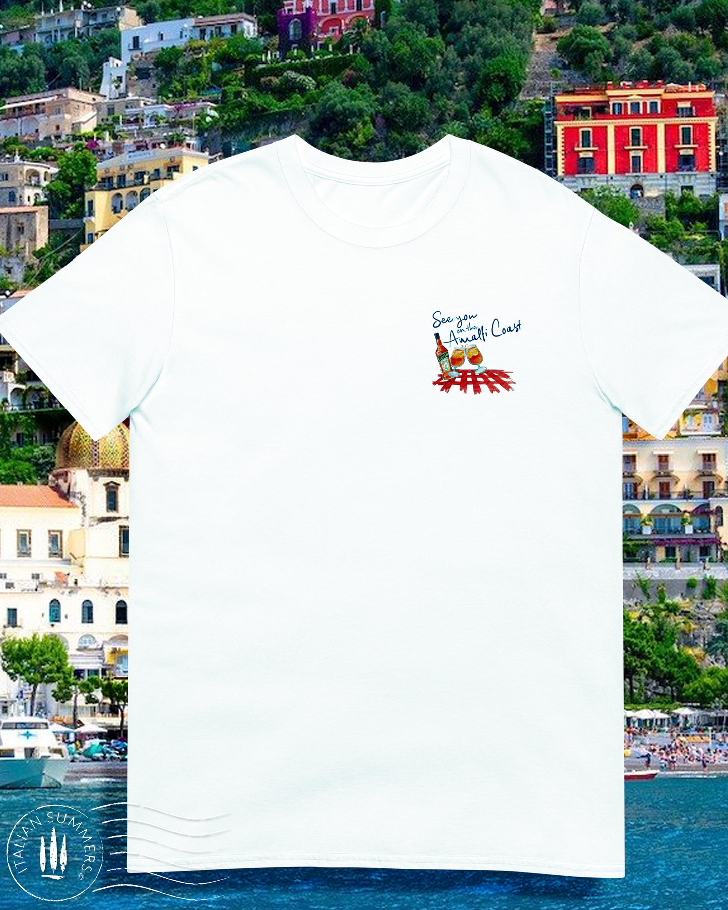 White cotton T shirt with an embroidered illustration on the left chest of two Aperol Spritz glasses in red-orange colors and a Aperol bottle on a red checkered tablecloth. Above, a Navy blue embroidered quote: See you on the Amalfi Coast.