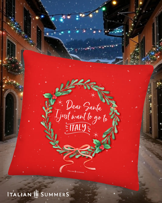 Red pillow with Italian Christmas design and text in front of a festive Italian village street scene.


