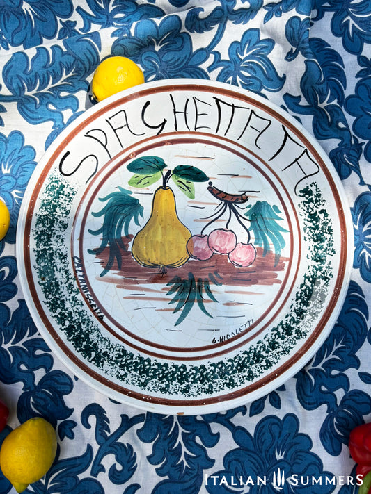 A large Sicilian vintage serving or Decorative plate with 'Spaghettata"' text and pear and cherries traditional Sicilian Maiolica  illustration, on a blue floral patterned background.