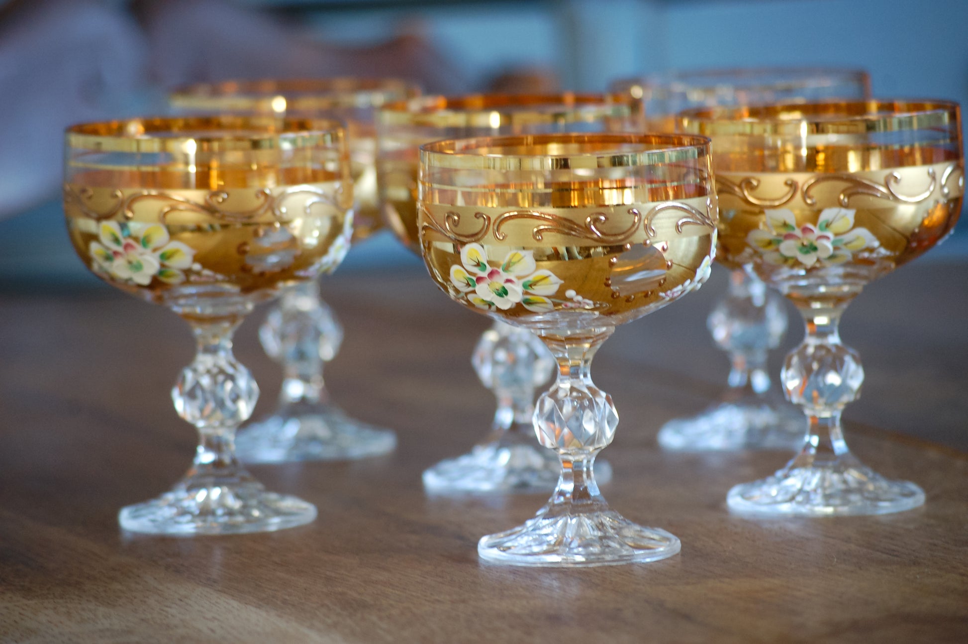 Set of ornate Murano wine glass goblets with gold rims and floral patterns on a wooden surface.