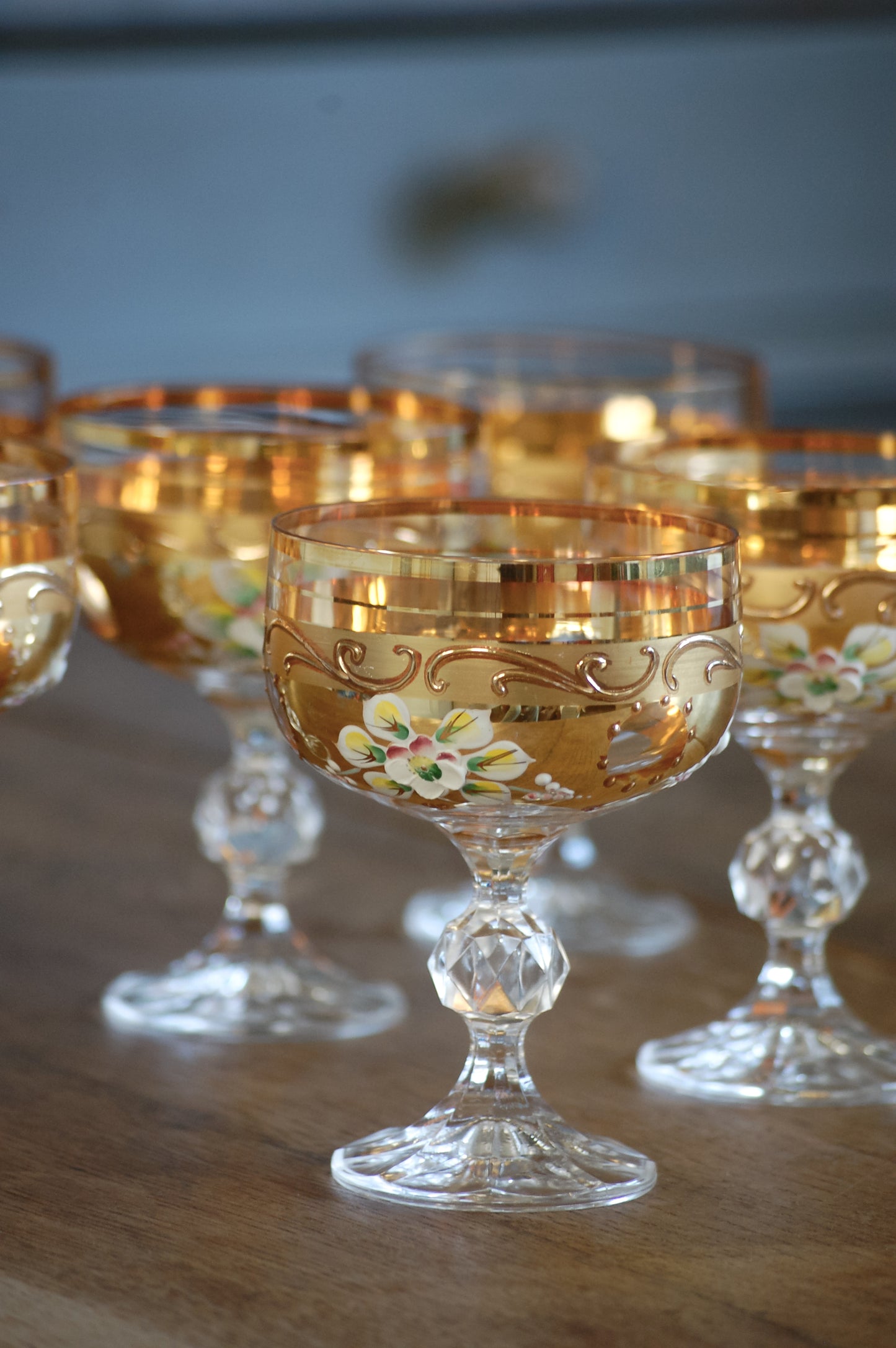 Decorative glass goblets with floral designs on gold, on a wooden surface.