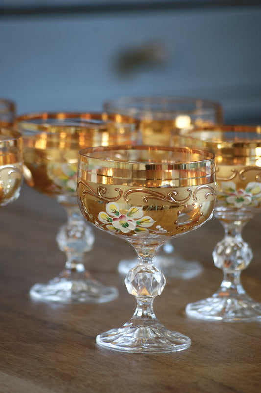 Decorative glass goblets with floral designs on gold, on a wooden surface.