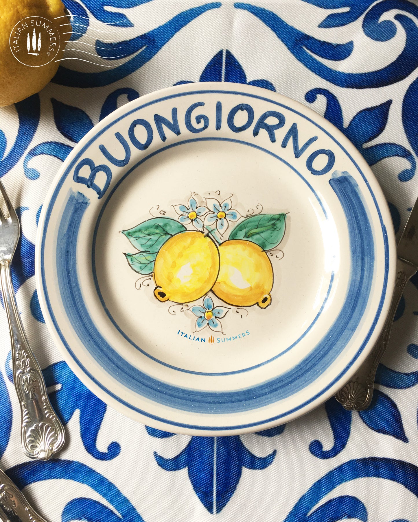 Ceramic plate Buongiorno Limoni handpainted in Sicily. This  plate has the quote Biongiorno on the rim - handpainted  - And colorfull lemons on the center of the plate  with lemon flowers. On the rim of the plate there are blue paint stripes. The blue color is ultra marine. This plate is designed and sold by Italian Summers.