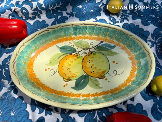A large oval serving or Decorative Sicilian ceramic plate with alemon design on a blue floral tablecloth, featuring traditional maiolica enamel colors in the 'fangotto' banding style reminiscent of baroque Sicily.