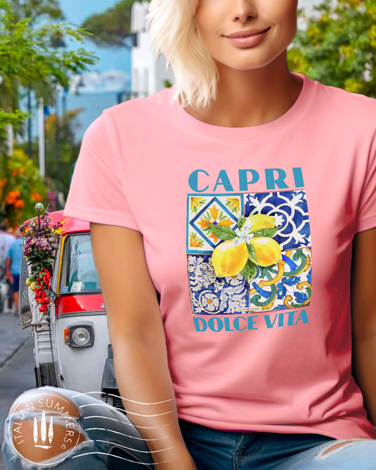 An all cotton T shirt with a Mediterranean tile design on the chest and a large cluster of Amalfi Coast lemons on top of the tiles. The lemons are bright yellow with green leaves and flowers. A blue text states: CAPRI DOLCE VITA
