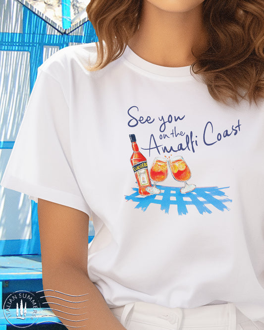 Italy inspired t-shirt with the quote See you in the Amalfi Coast. Featuring a hand drawn sketch of a bottle of Aperol Spritz and two glasses on a brigt blut table cloth. Designed and sold by Italian Summers