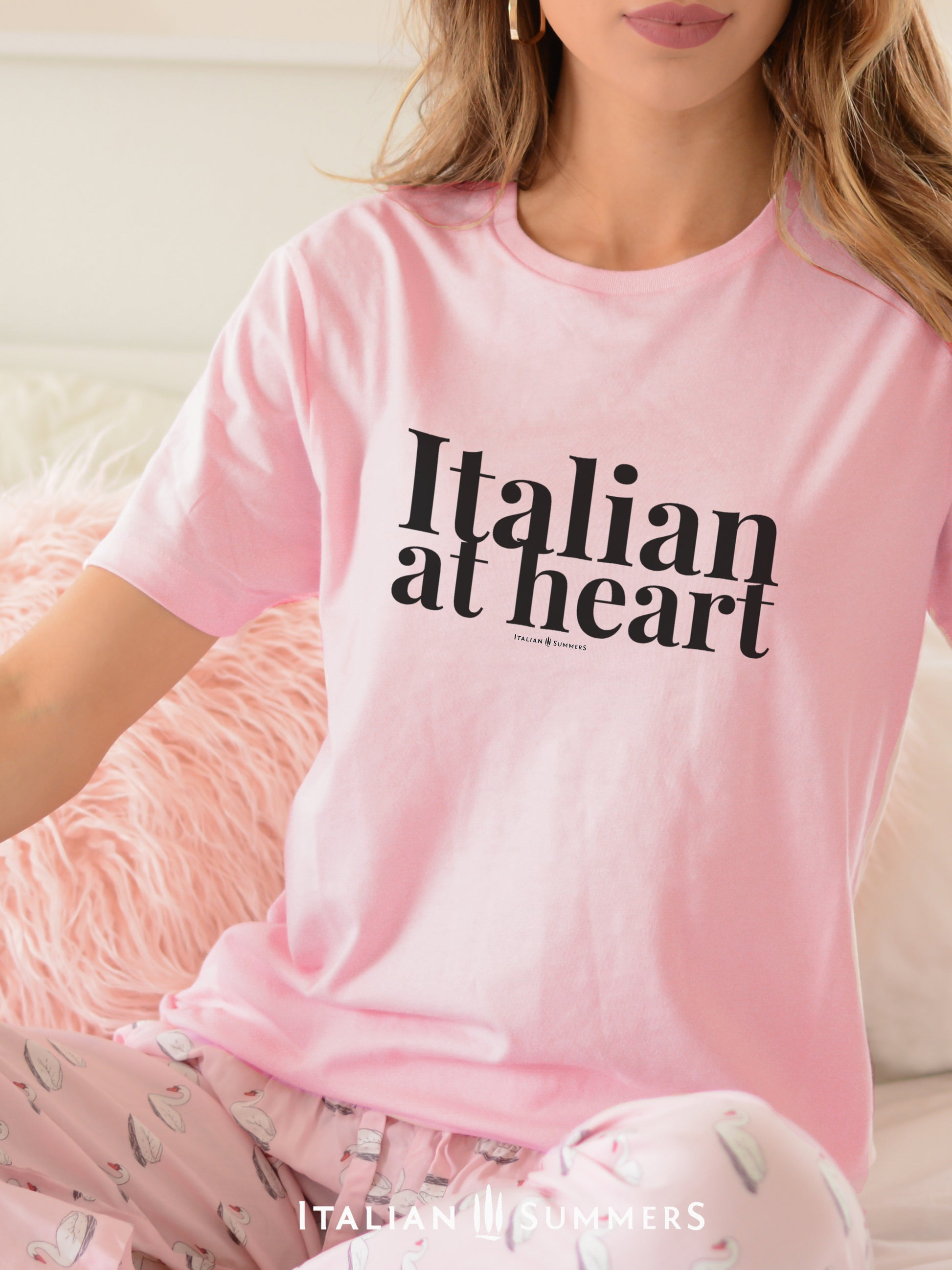 A woman sitting on a couch wearing a soft pink T shirt with the text ITALIAN AT HEART in large black letters on the chest