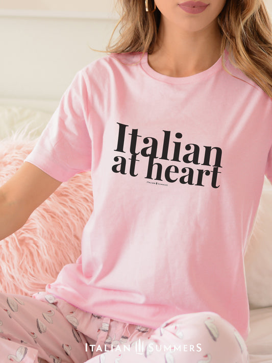 A woman sitting on a couch wearing a soft pink T shirt with the text ITALIAN AT HEART in large black letters on the chest