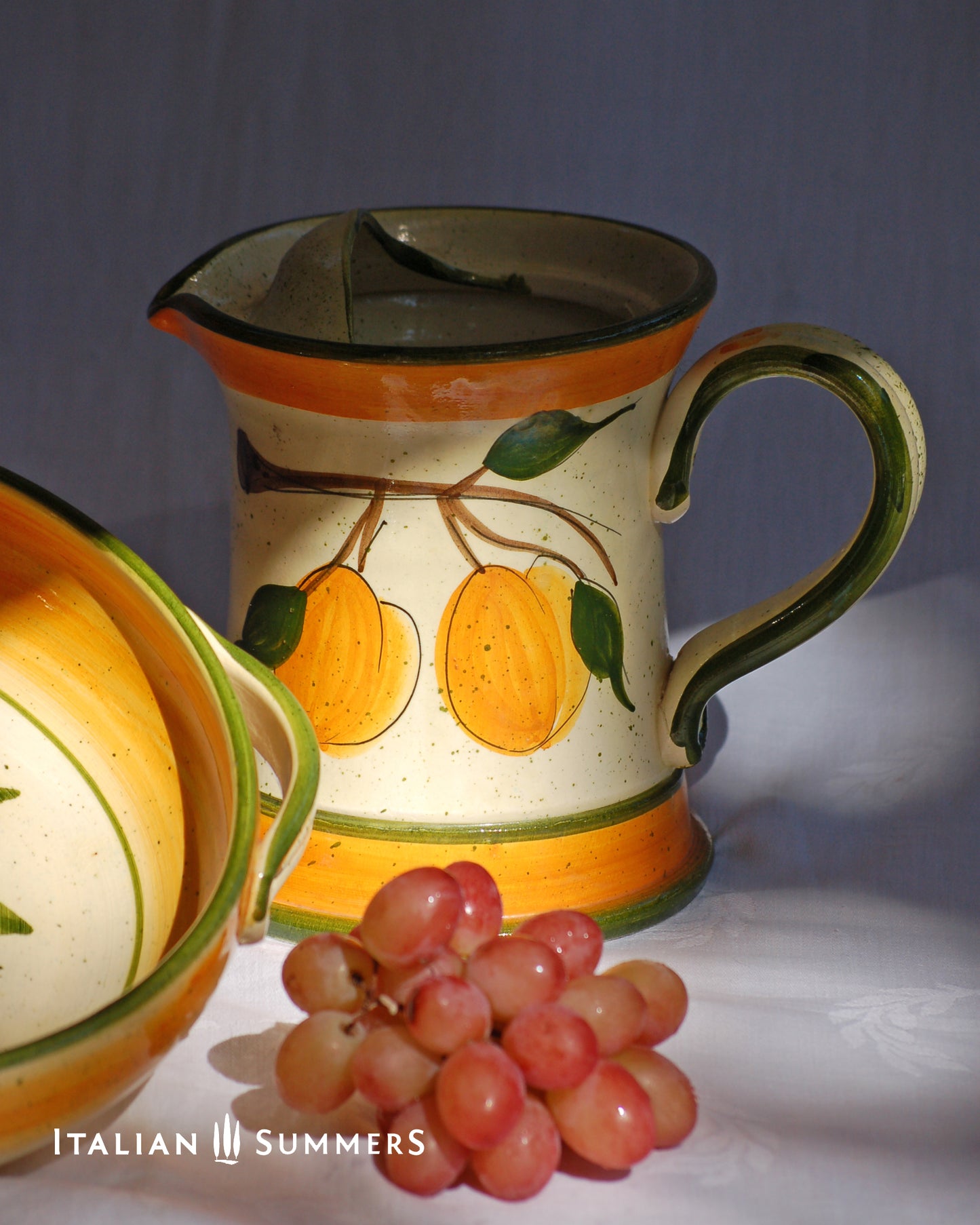 Ceramic pitcher with fruit design and grapes on a gray background, featuring 'Italian Summers' branding.
