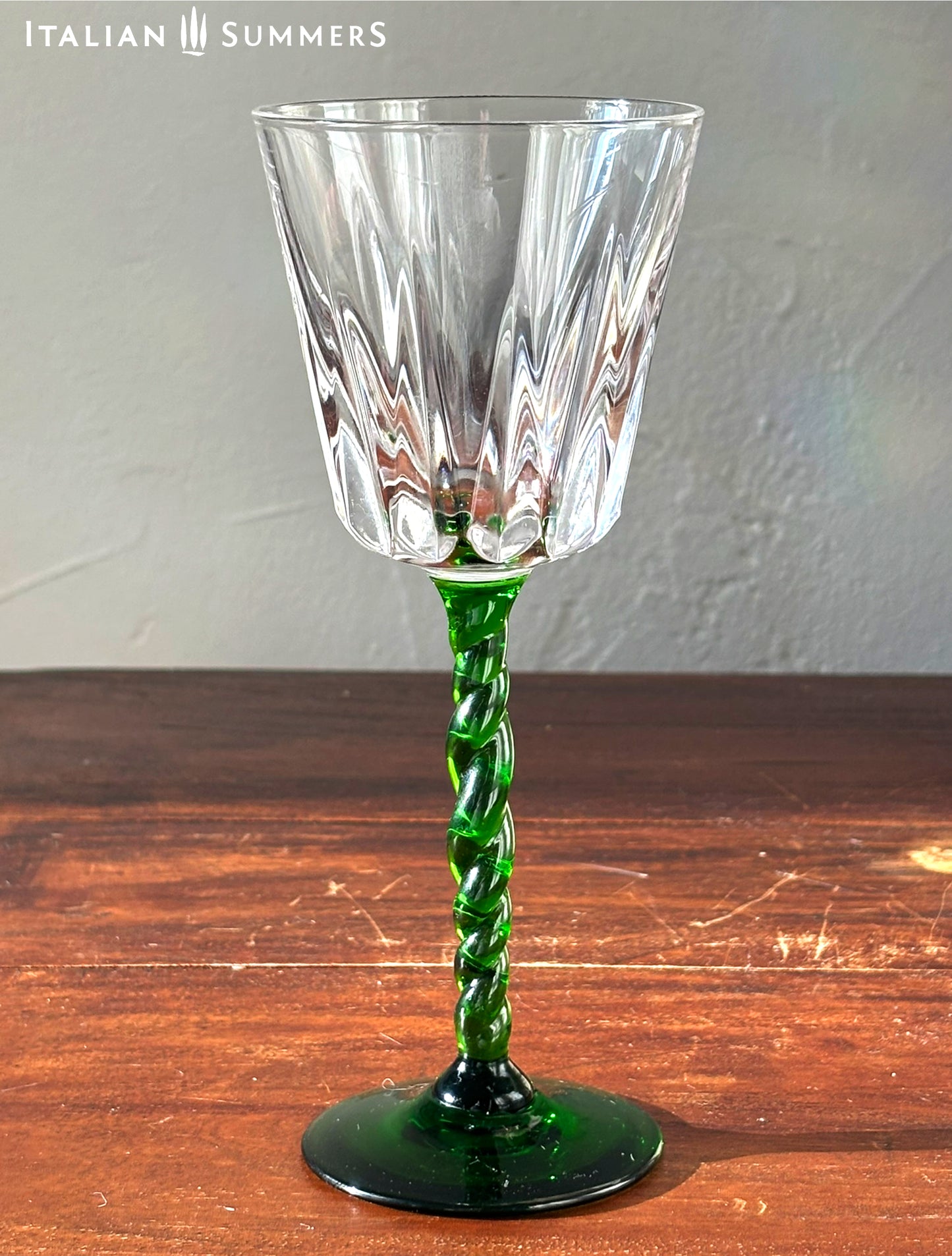 Glass goblet with green stem on a wooden surface, brand 'Italian Summers' visible