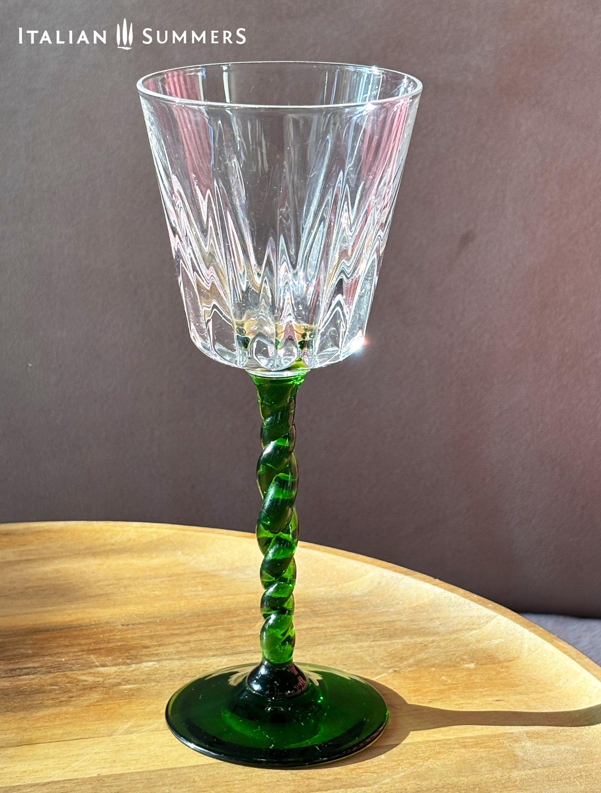 Crystal wine glass with a green spiral stem on a wooden surface, branded 'Italian Summers'.